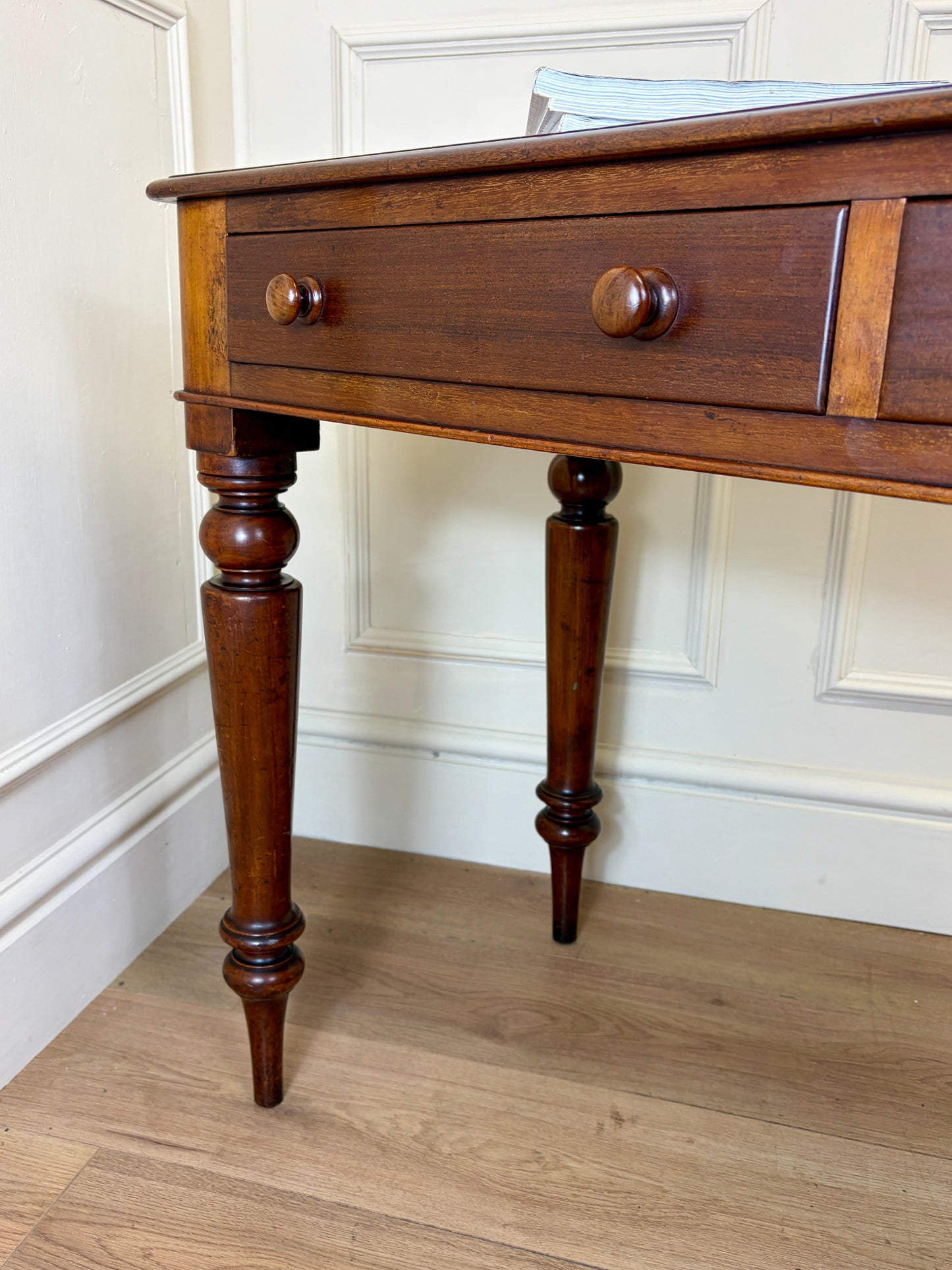 Wooden side table with a single drawer against a white paneled wall.