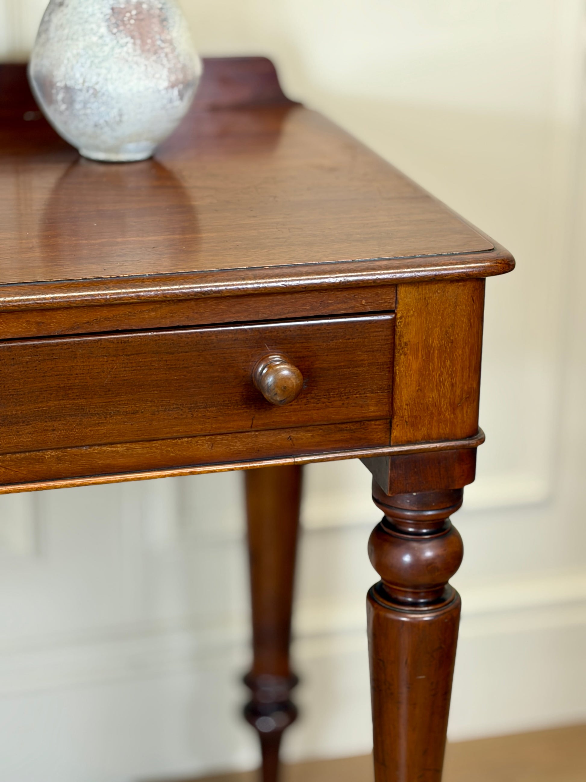 Wooden side table with a single drawer and a vase on top against a neutral background