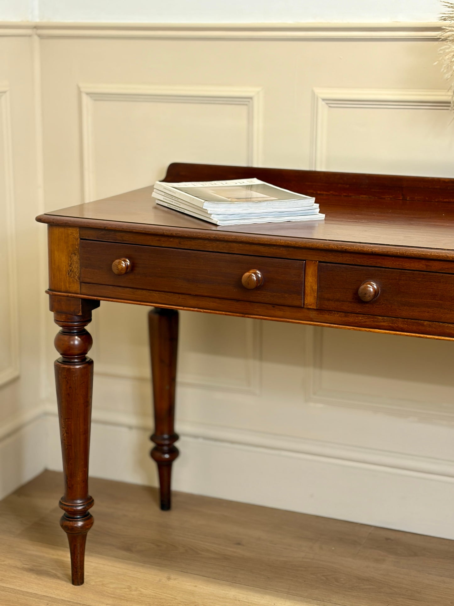Wooden desk with two drawers against a white paneled wall.