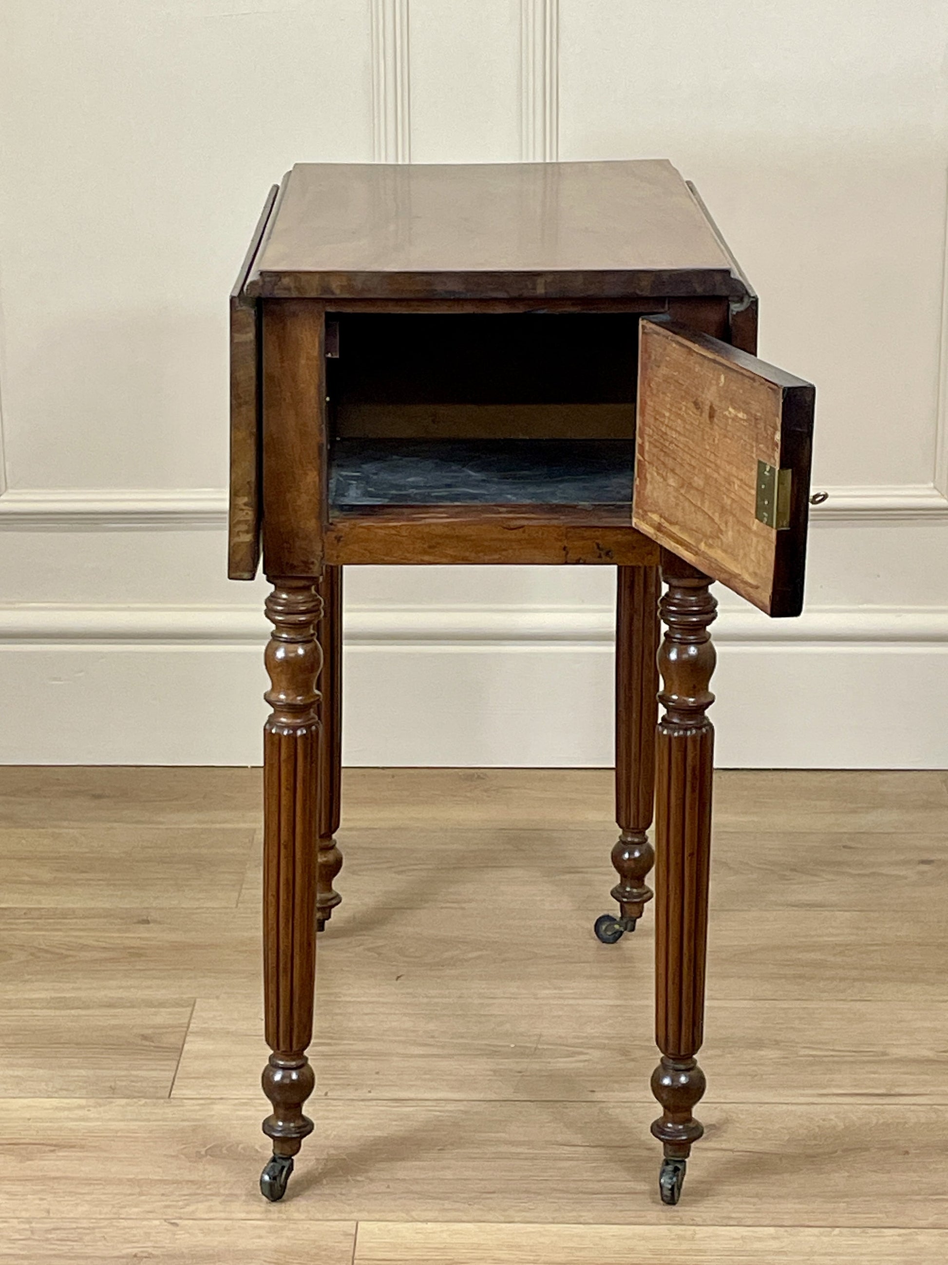 Wooden side table with a drawer open on a wooden floor against a white wall.