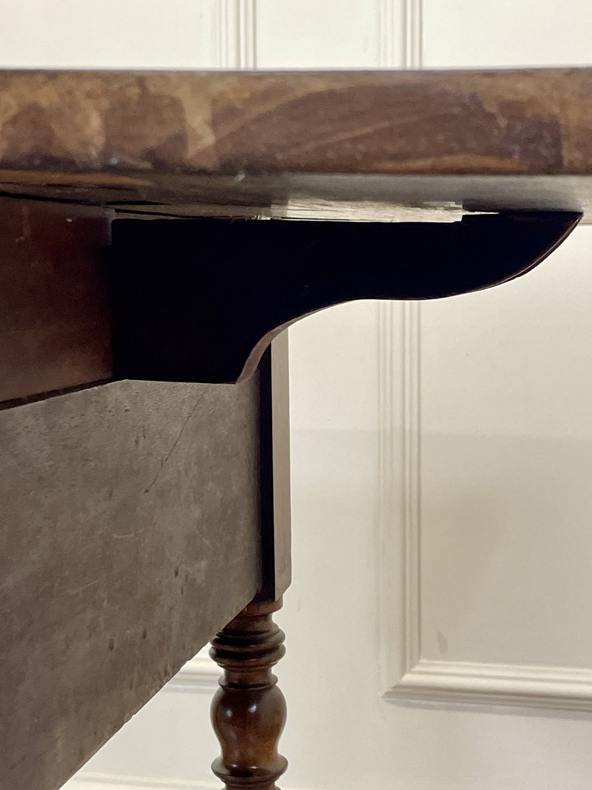 Close-up of a wooden table with a marble top against a white paneled wall.