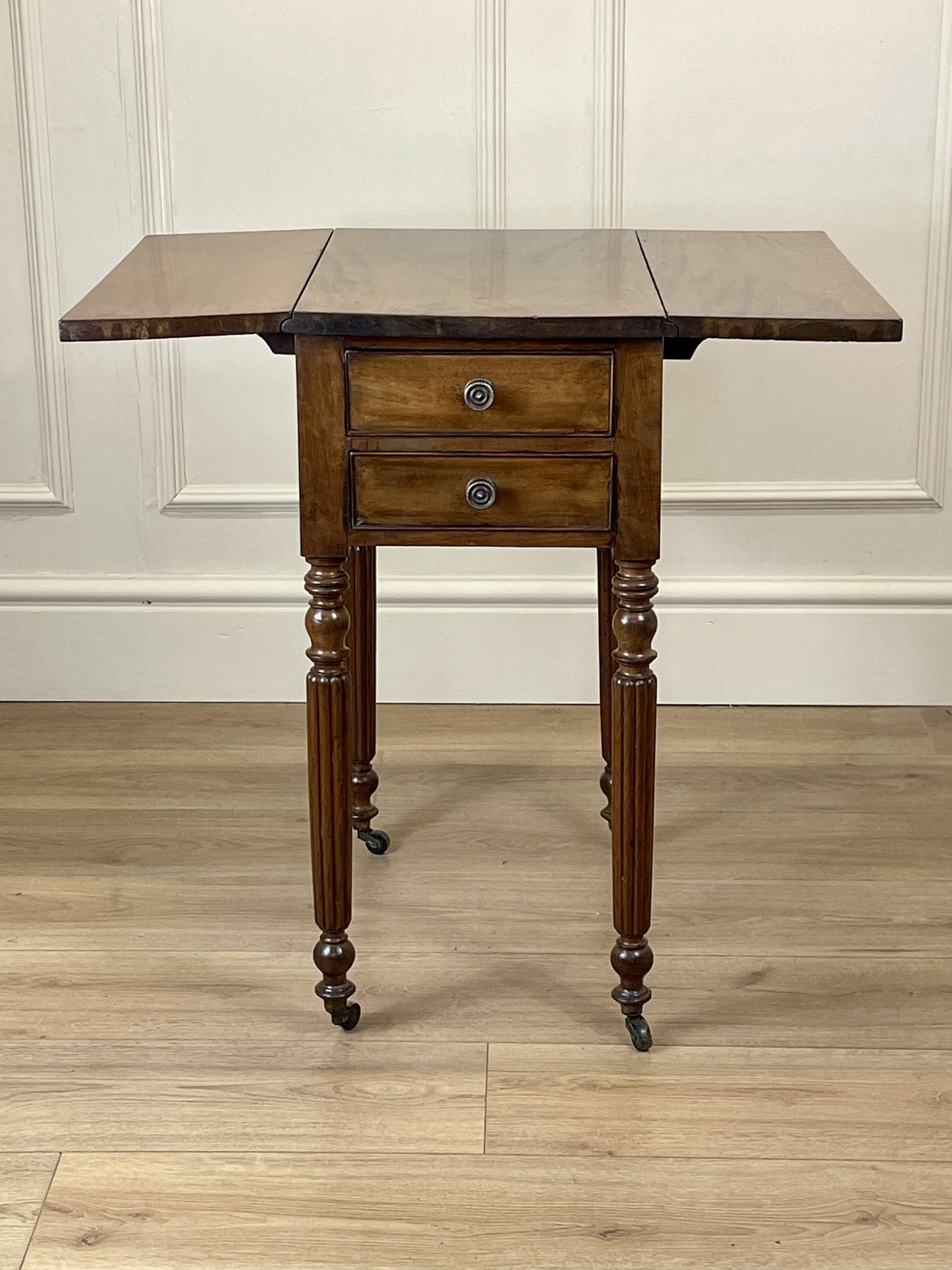 Wooden table with a single drawer on a wooden floor against a white paneled wall.