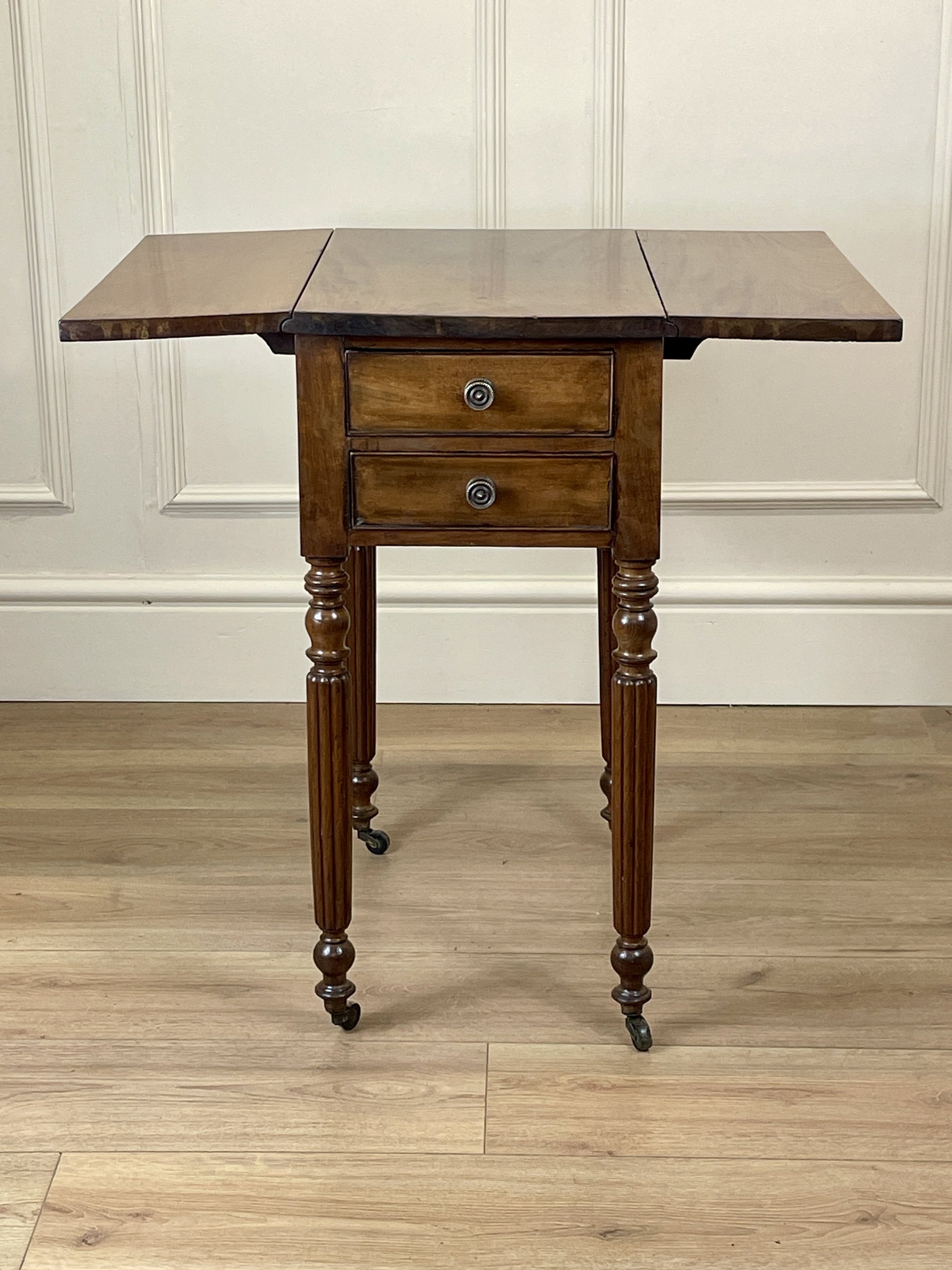 Wooden table with a single drawer on a wooden floor against a white paneled wall.