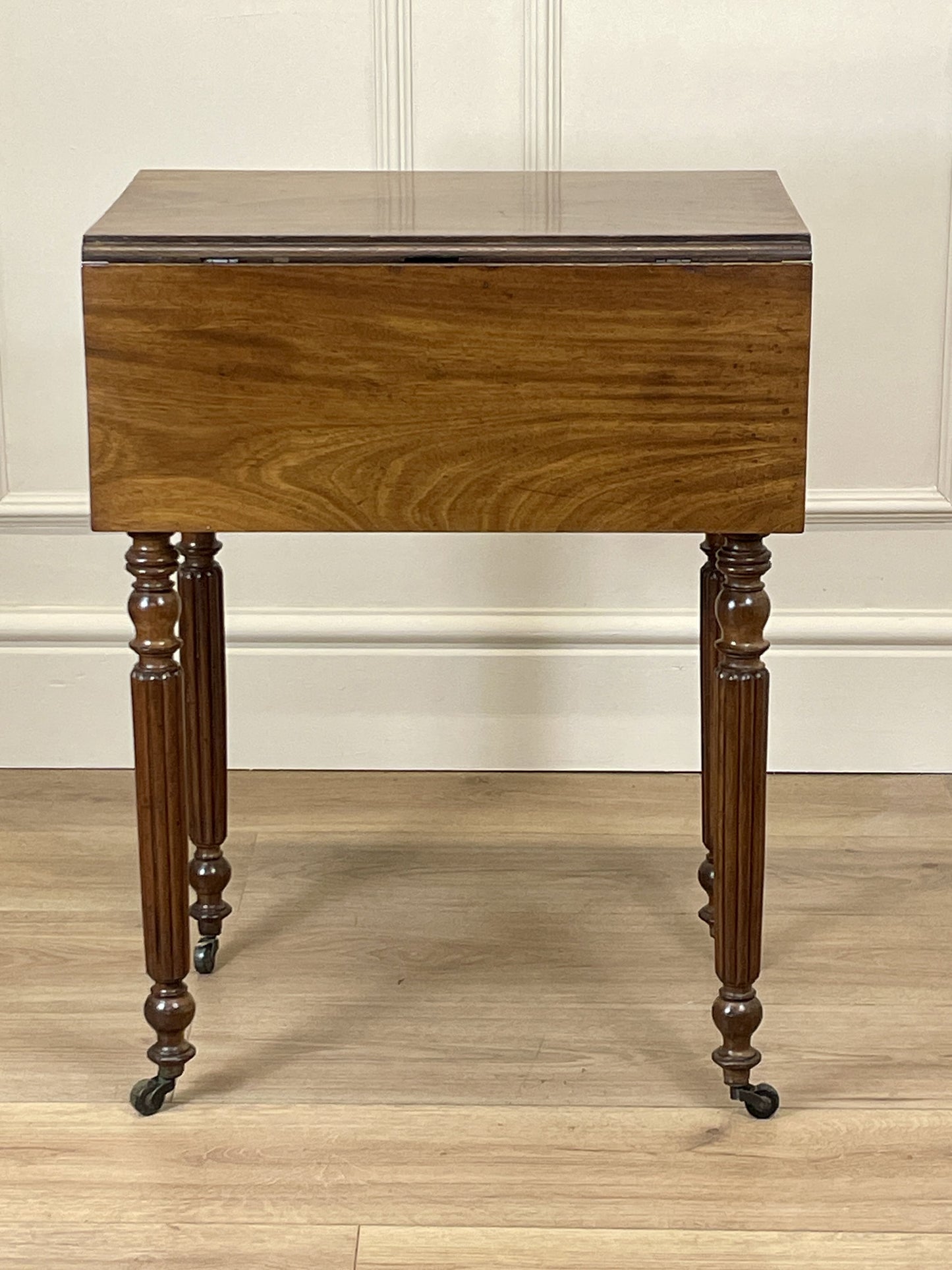 Wooden side table with a drawer on a wooden floor against a white wall.
