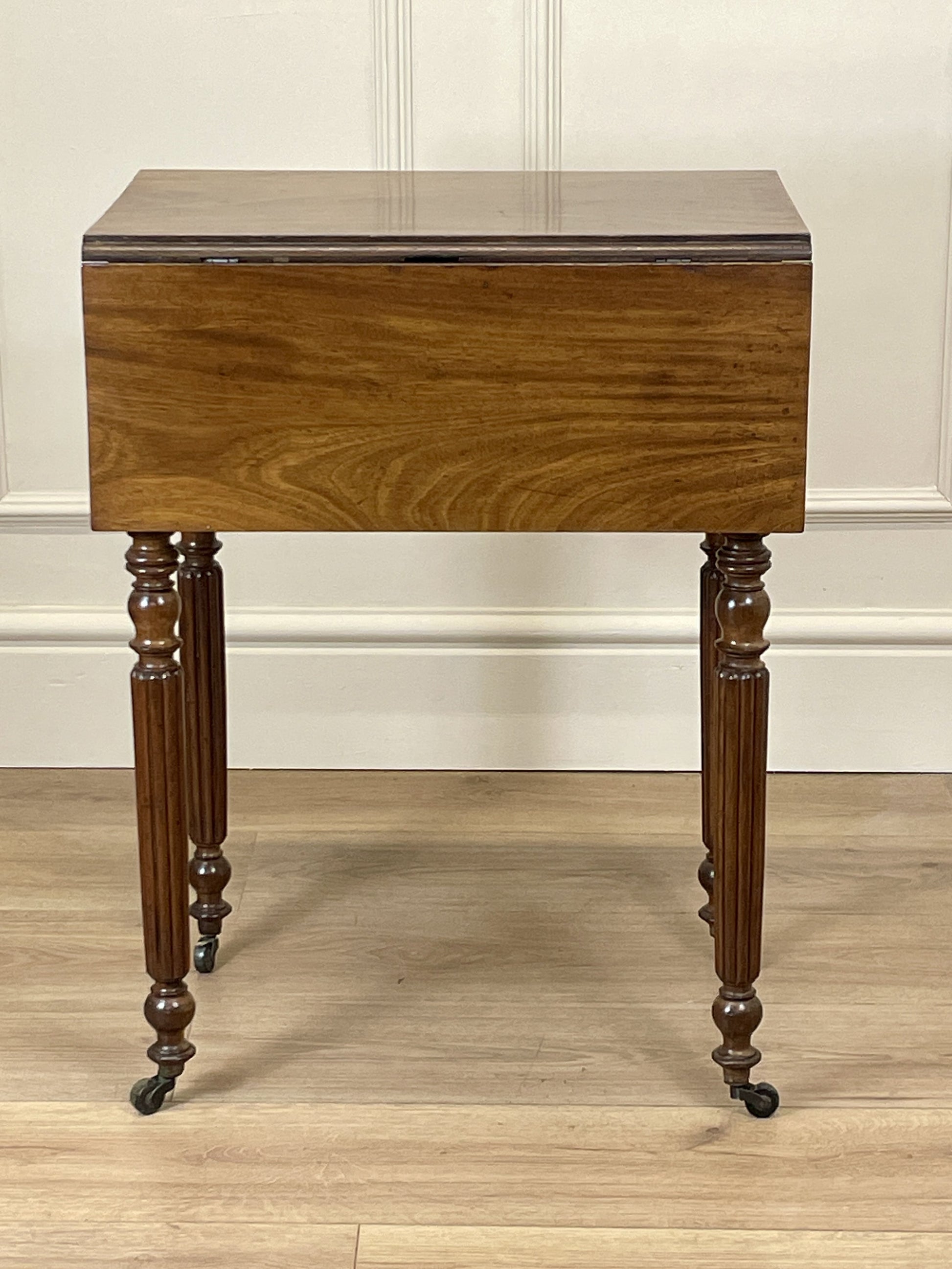 Wooden side table with a drawer on a wooden floor against a white wall.