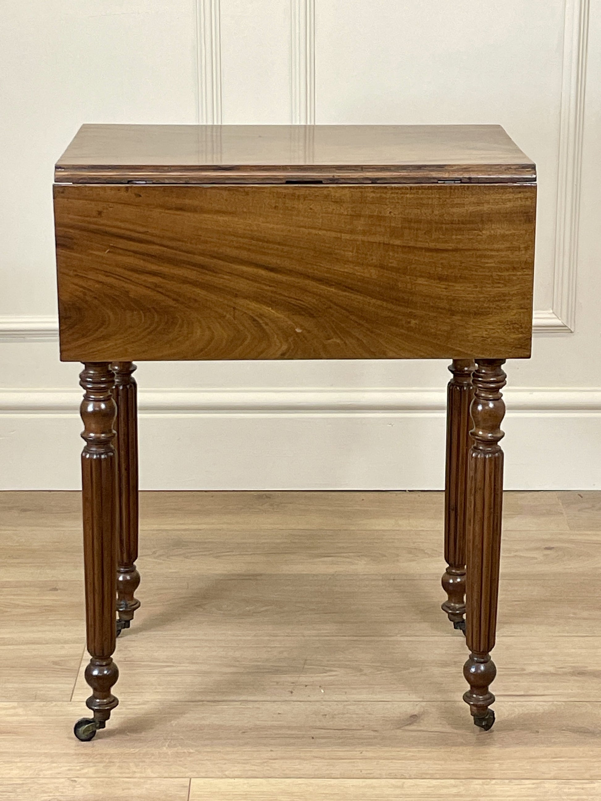Wooden side table with a single drawer on a wooden floor against a white wall.