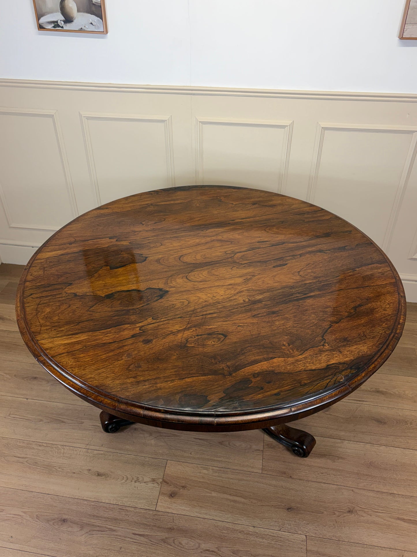 Round wooden table in a room with panelled walls and a light wood floor.