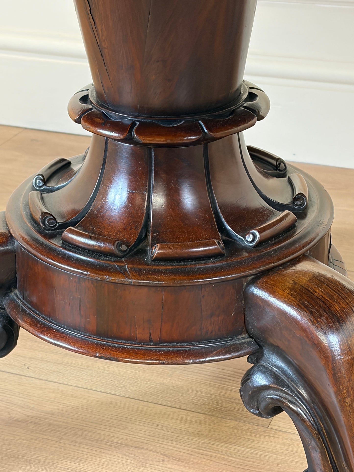 Close-up of a wooden pedestal with intricate carvings on a light wood floor.
