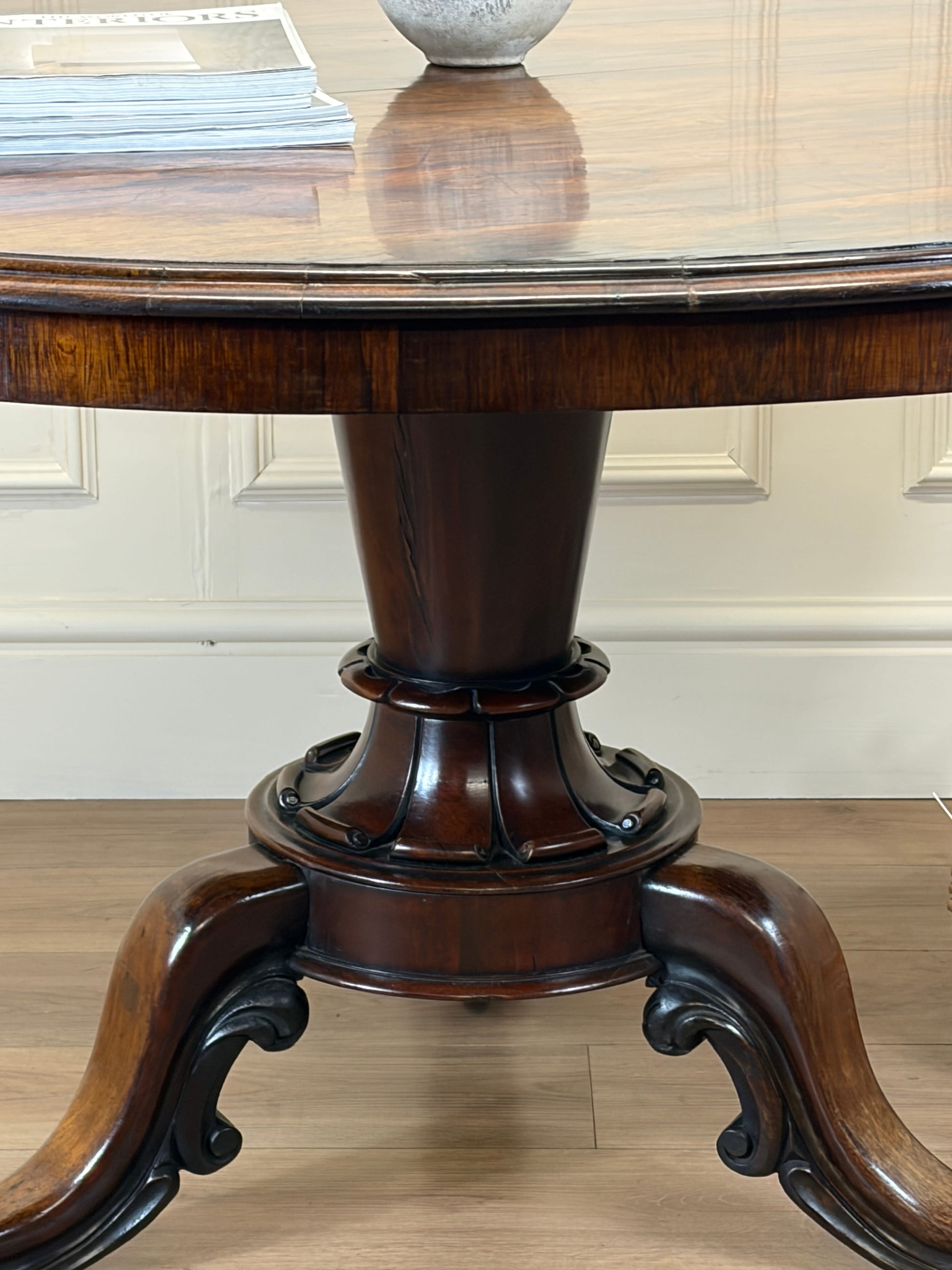 Wooden pedestal table with a reflective surface on a wooden floor.