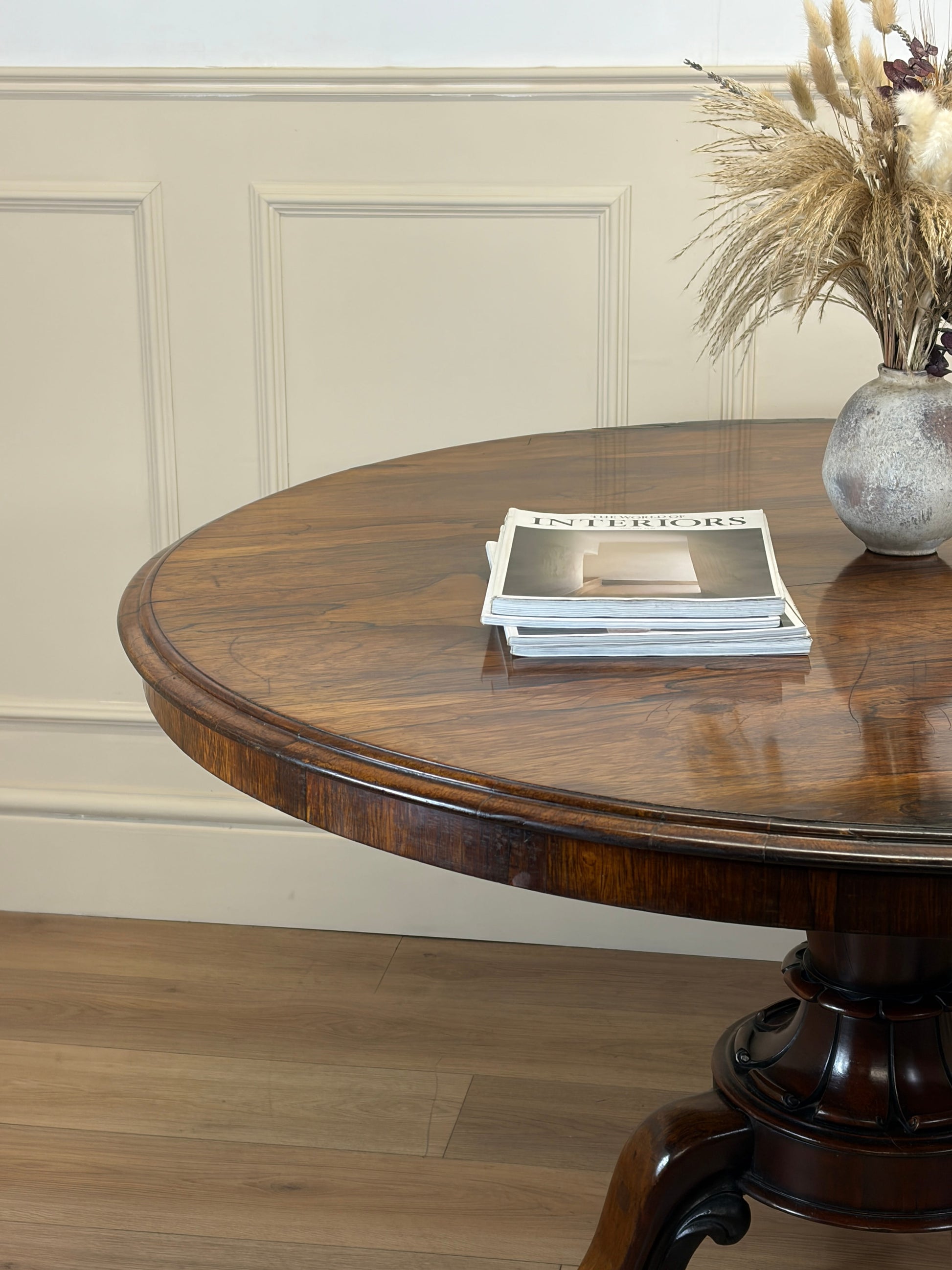 Round wooden table with a vase of flowers and books on a light-colored wall background