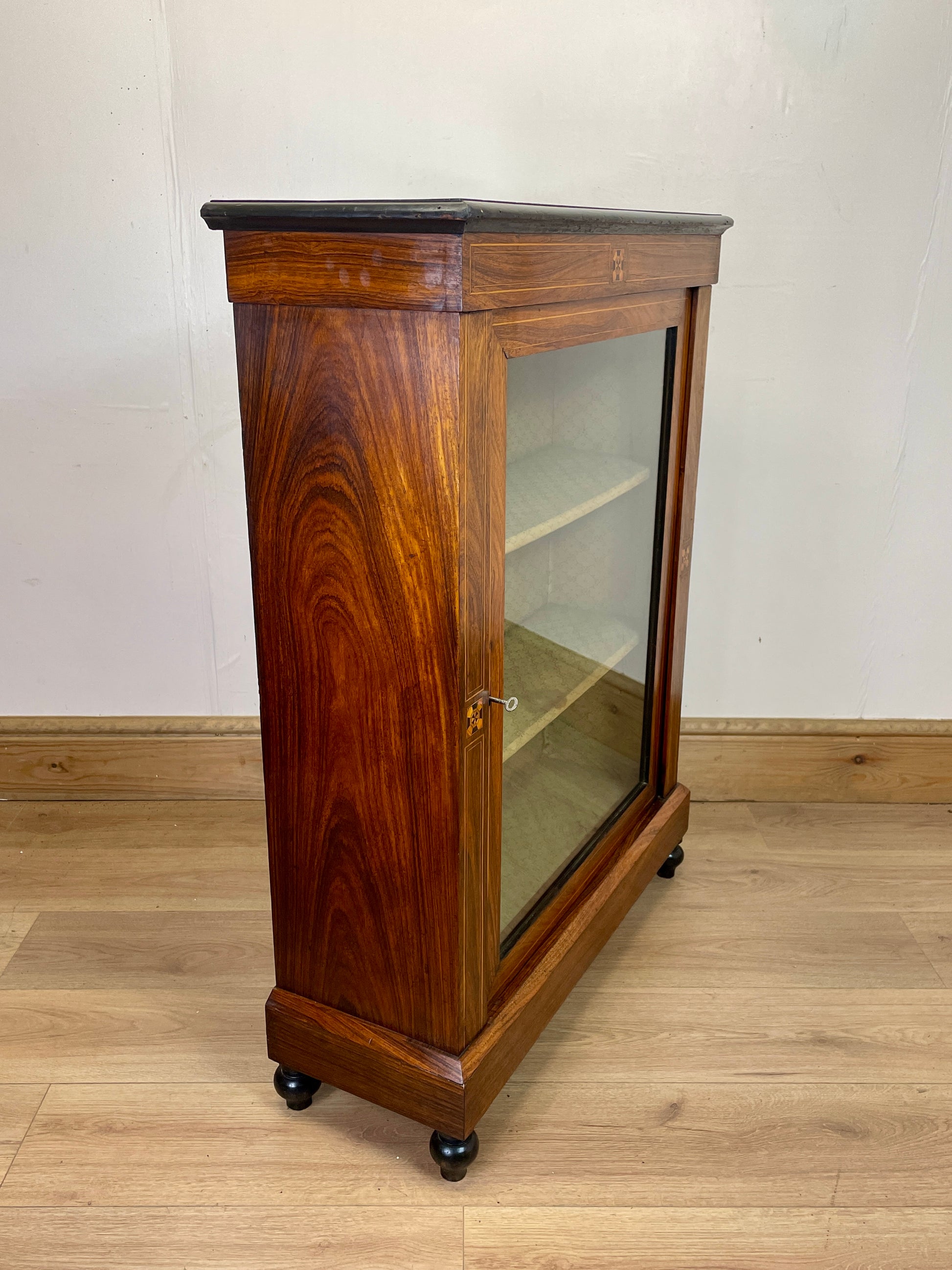 Wooden display cabinet with glass door on a wooden floor against a white wall