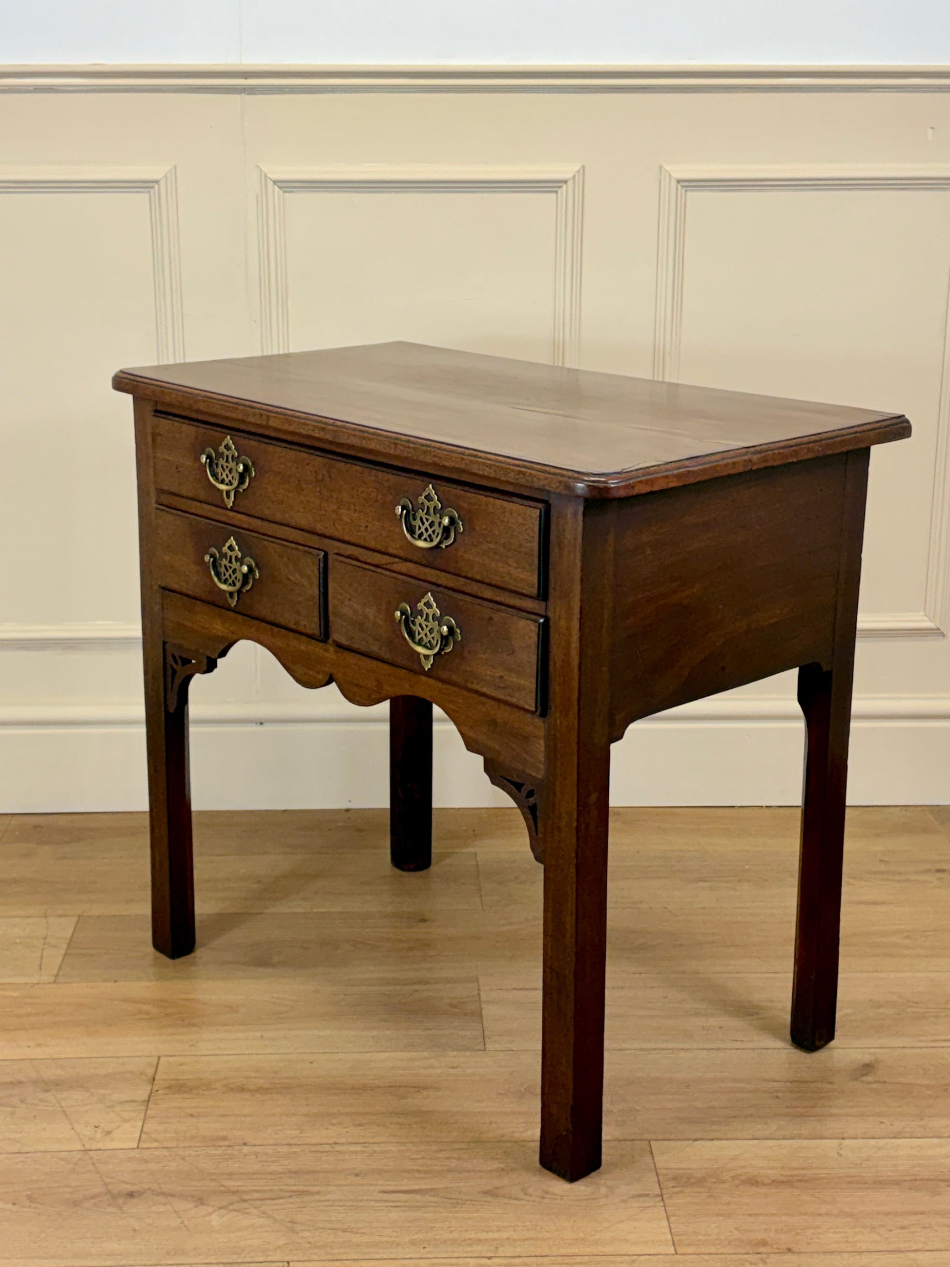 Wooden side table with two drawers against a beige paneled wall.