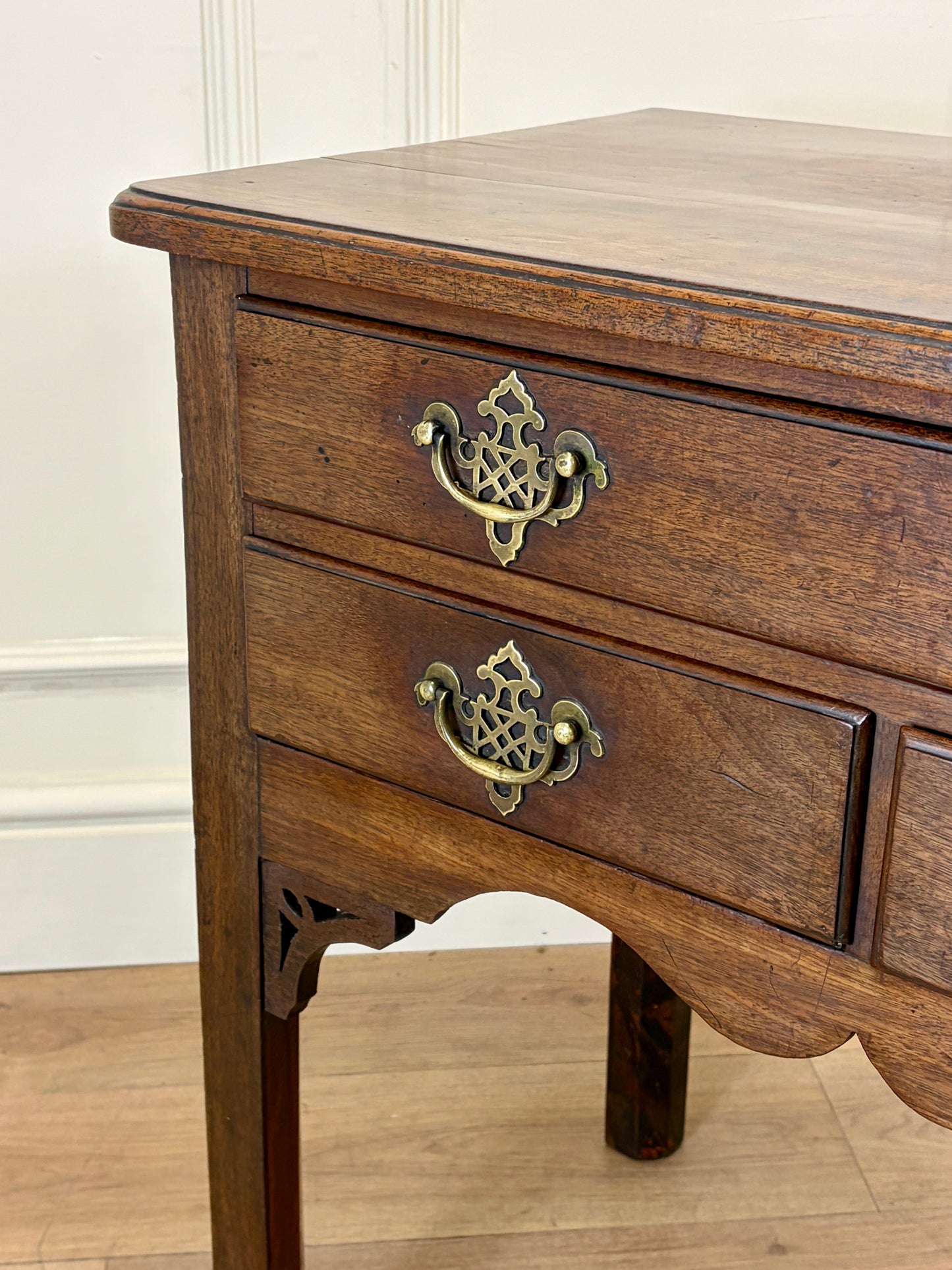 Wooden side table with brass handles on a wooden floor.