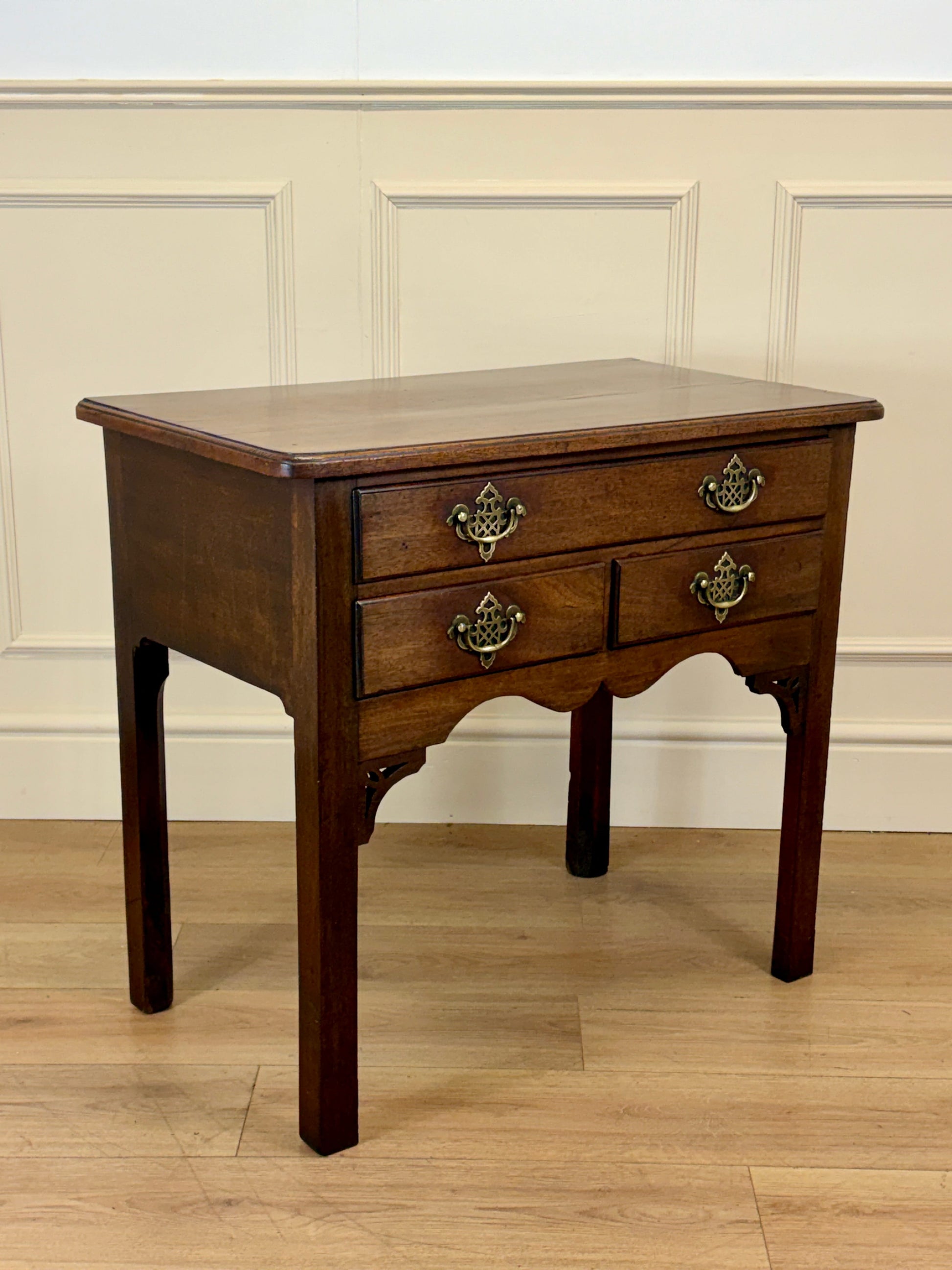 Wooden side table with two drawers against a beige wall.