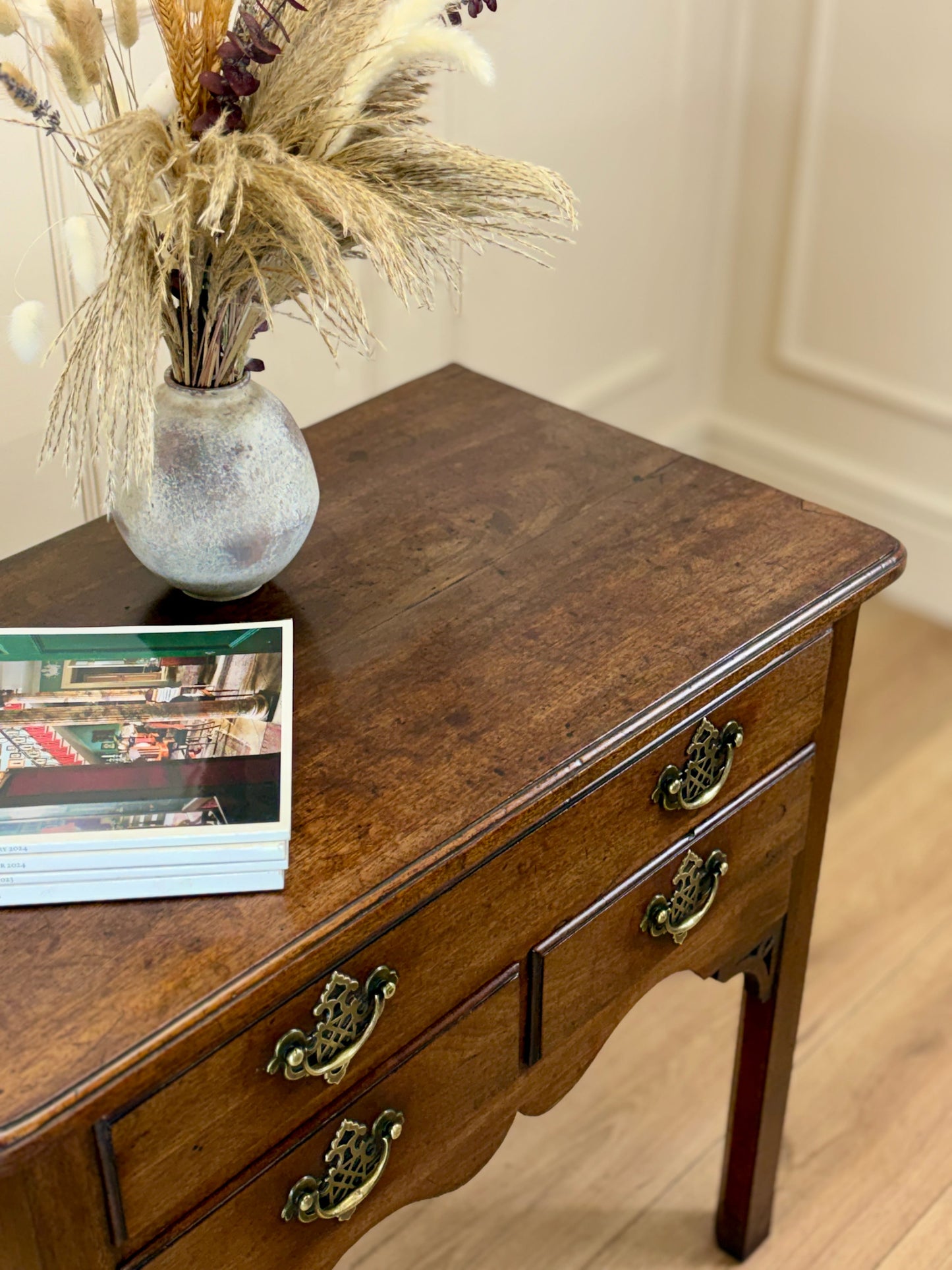 Wooden side table with a vase of dried plants and books on a light wood floor.