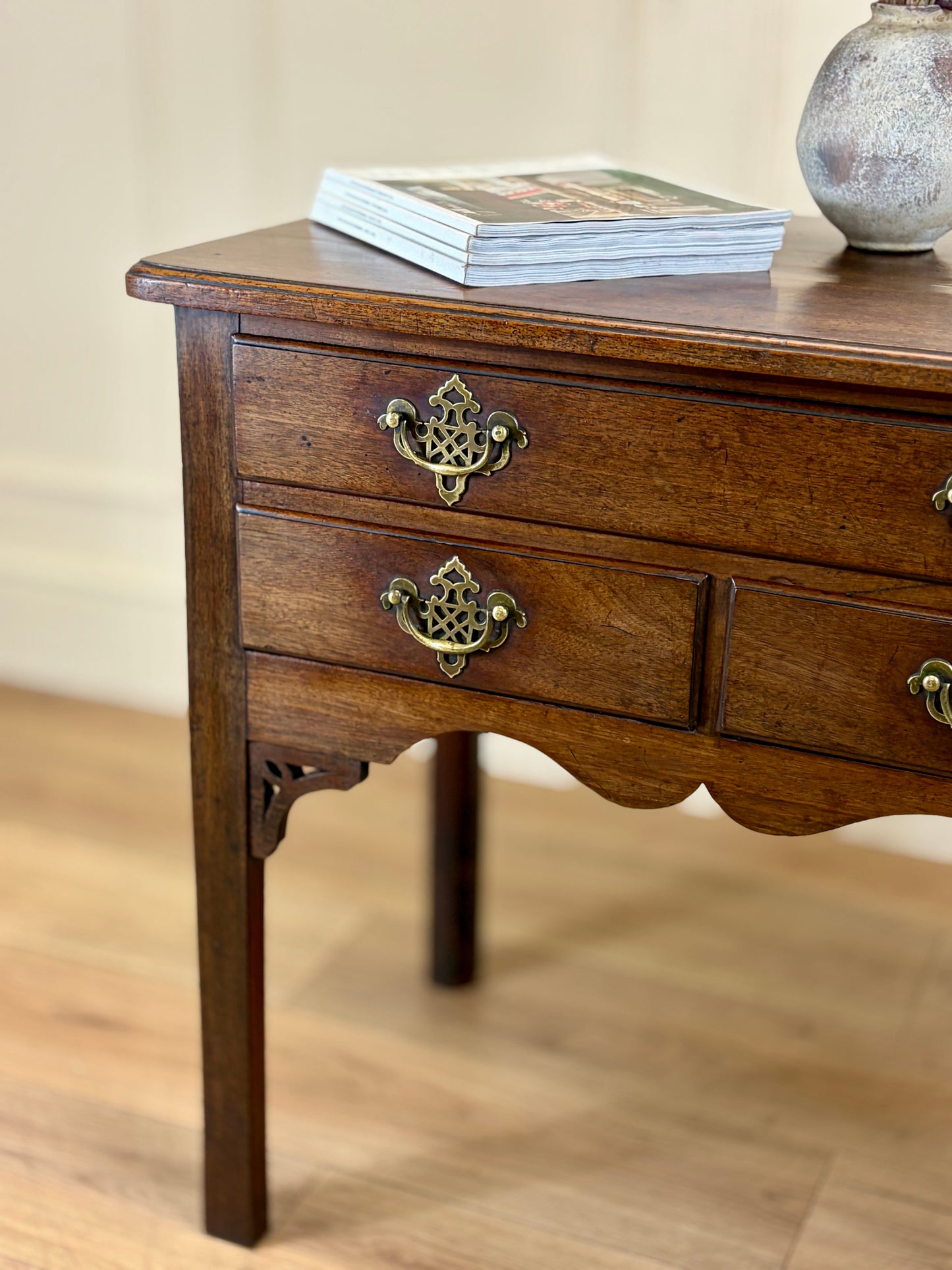 Wooden side table with two drawers and decorative handles on a wooden floor.