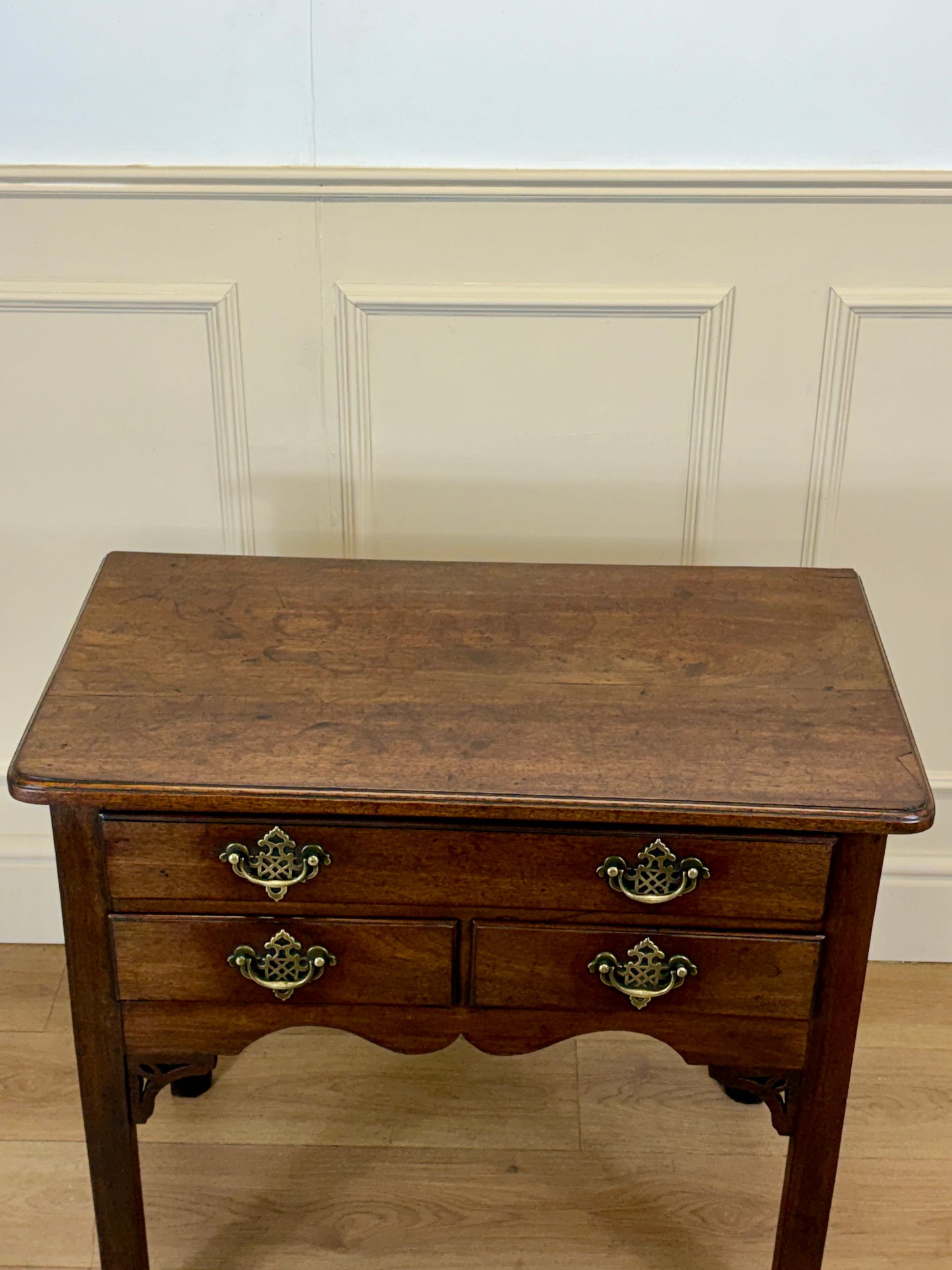 Wooden side table with two drawers against a white paneled wall.