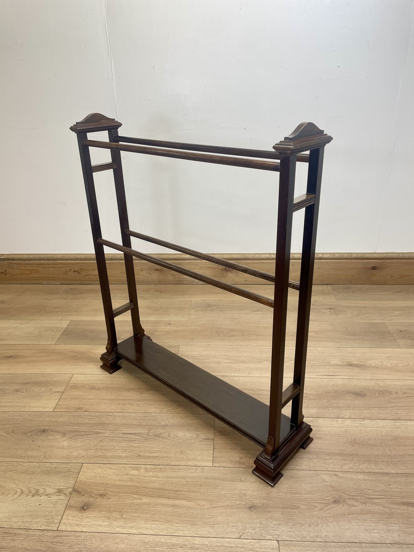 Wooden garment rack on a wooden floor with a white wall background