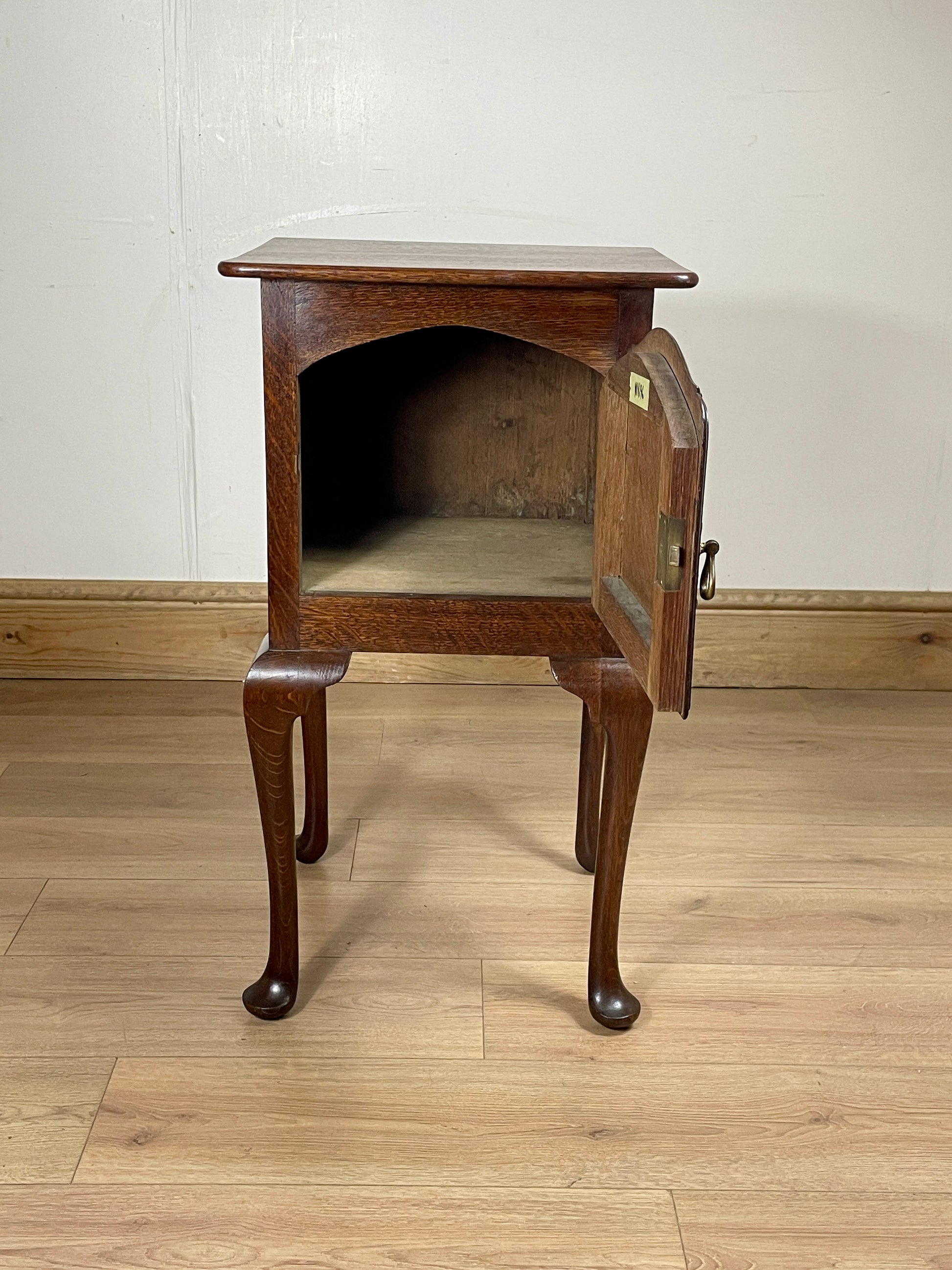 Wooden side table with a drawer on a wooden floor against a white wall