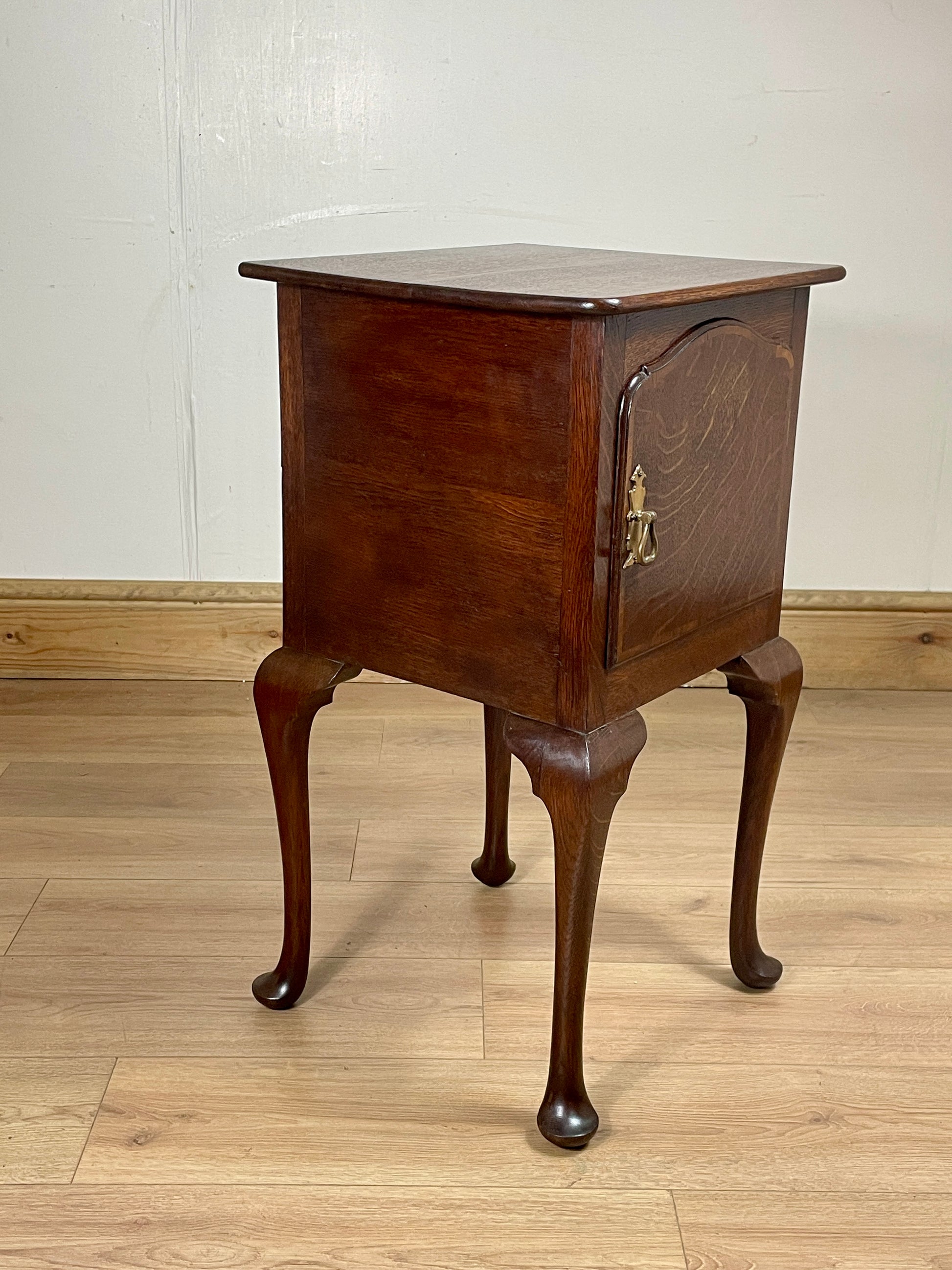 Wooden side table with a single drawer on a wooden floor against a white wall