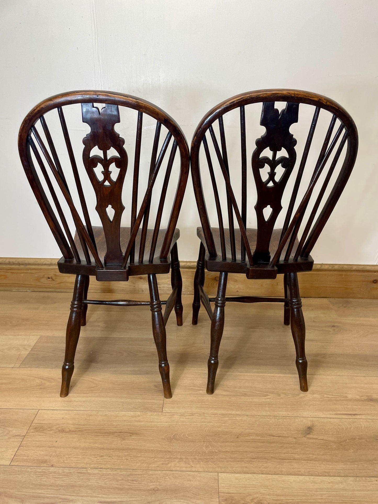 Two wooden chairs with intricate back designs on a wooden floor.
