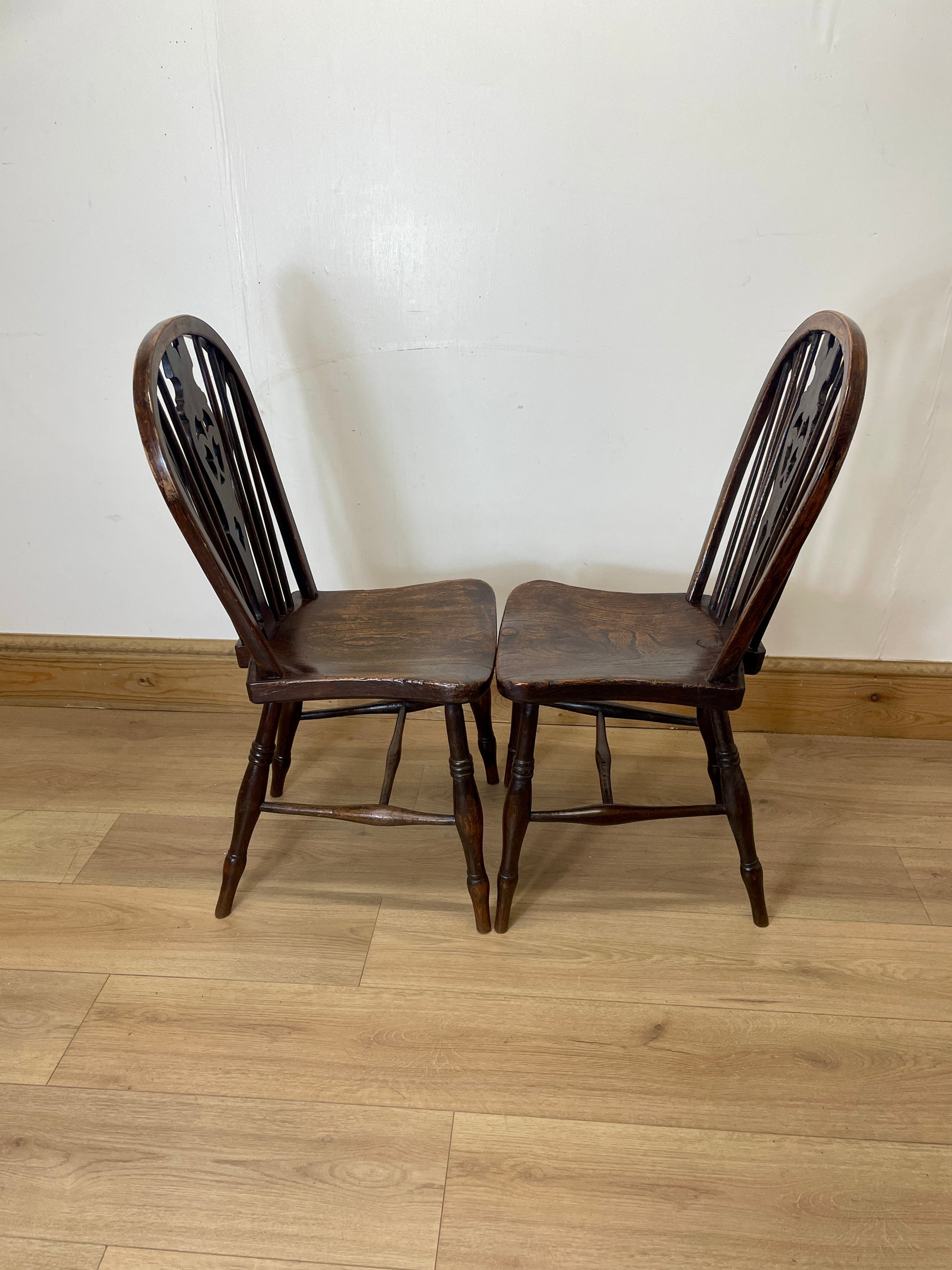 Two wooden chairs on a wooden floor with a white wall background