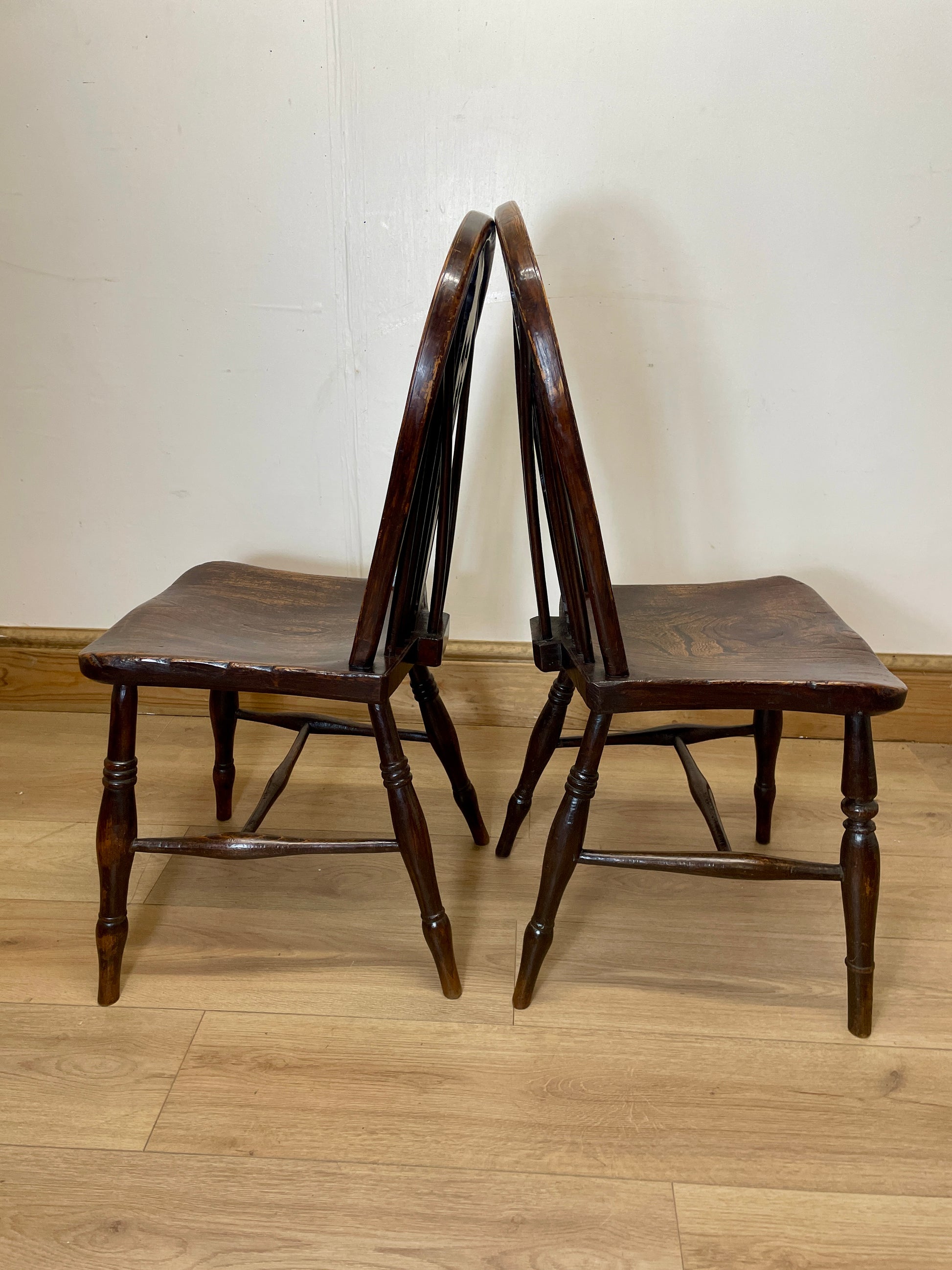 Two wooden chairs on a wooden floor against a white wall