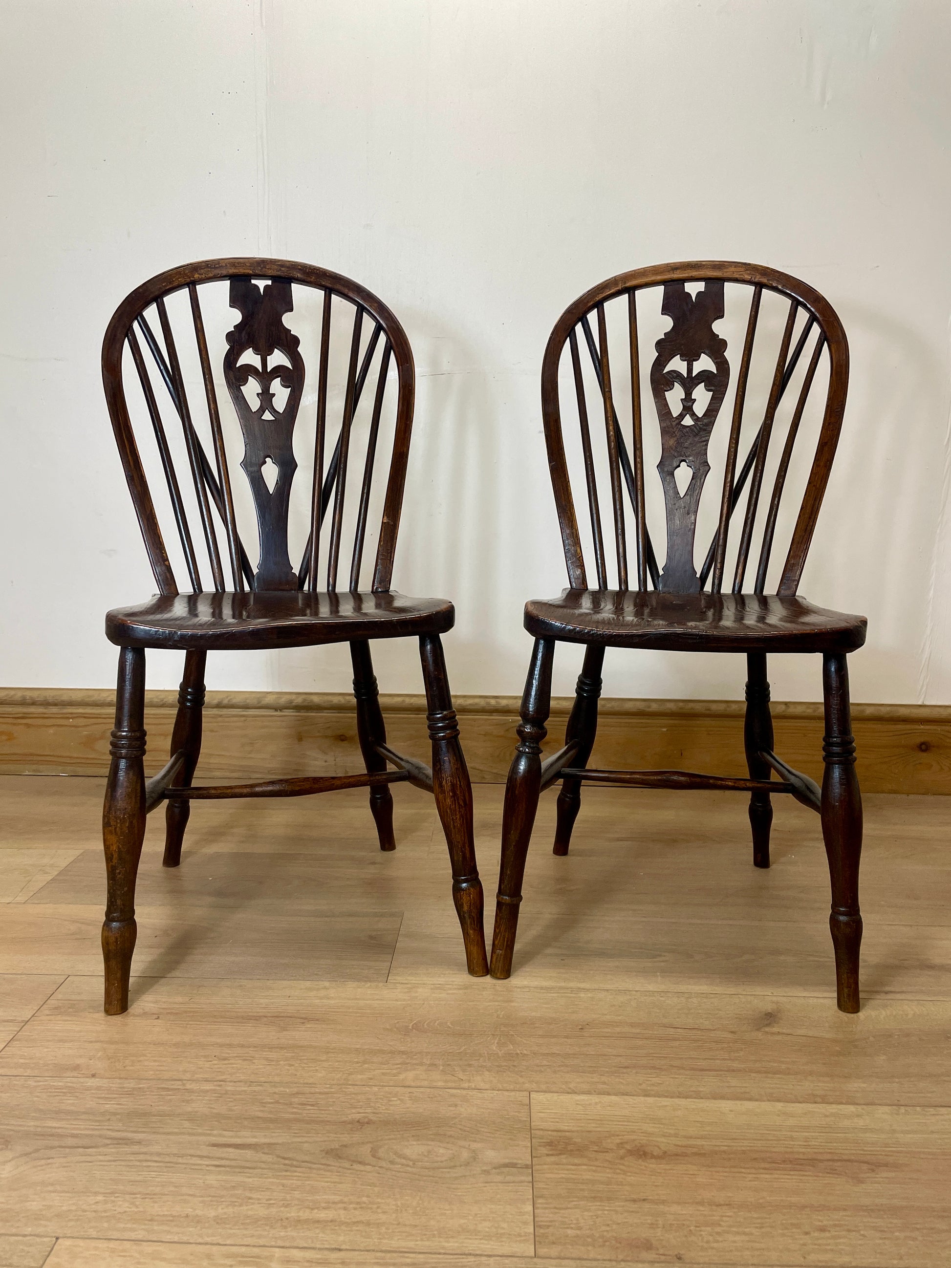 Two wooden chairs with decorative backrests on a wooden floor.