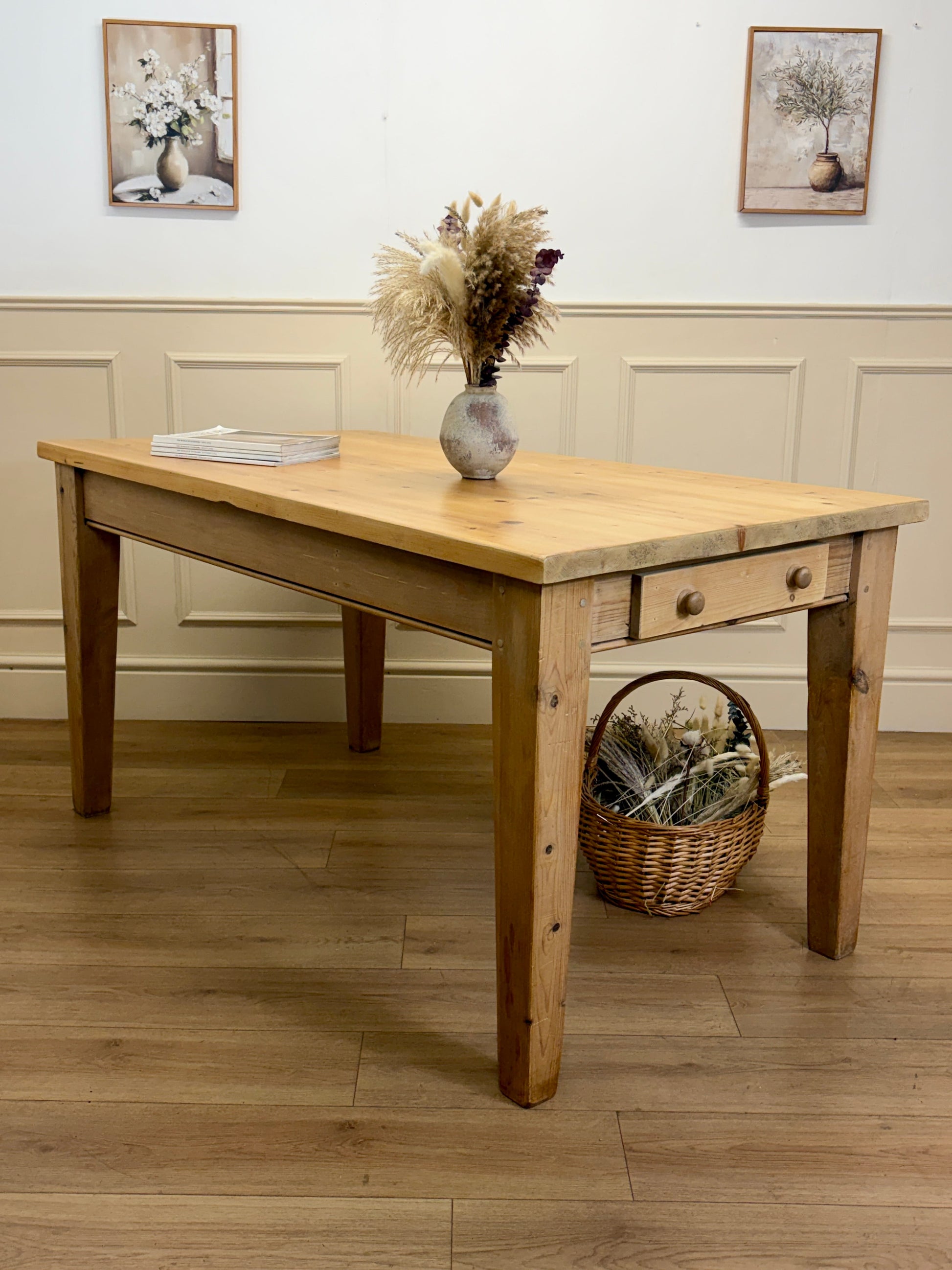 Wooden dining table with a vase of flowers and a basket on a wooden floor.