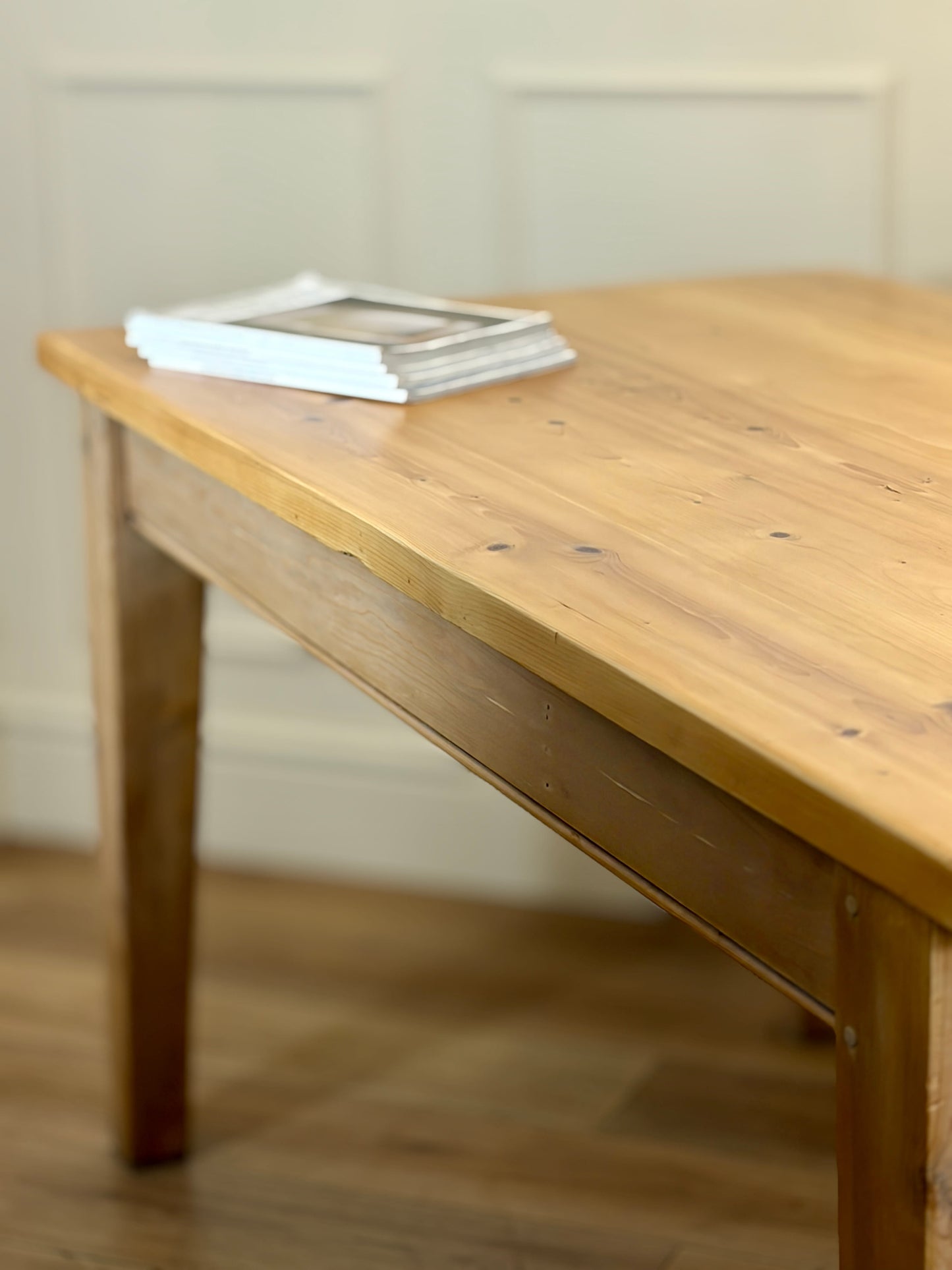 Wooden table with a stack of books on a wooden floor.
