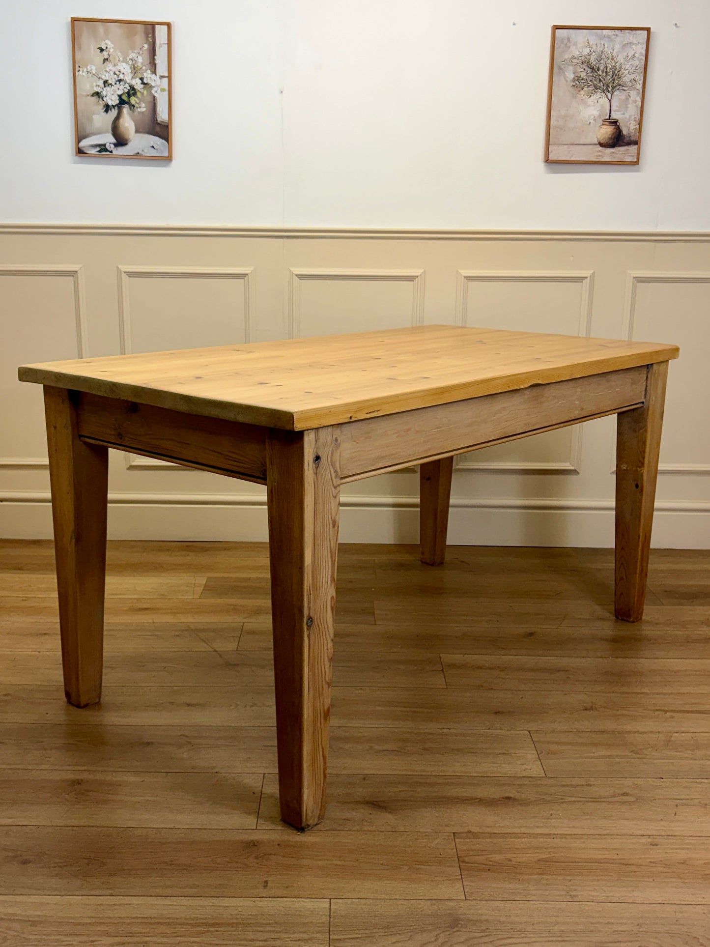 Wooden dining table in a room with wainscoting and framed pictures.