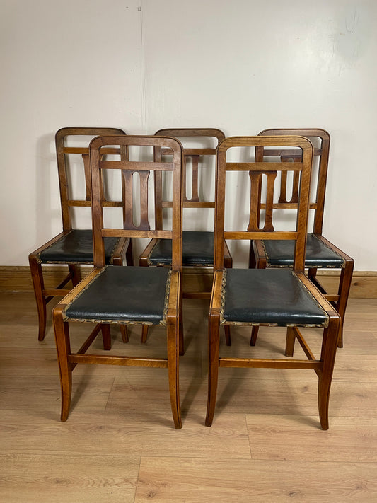 Set of six wooden chairs with black seats on a wooden floor.