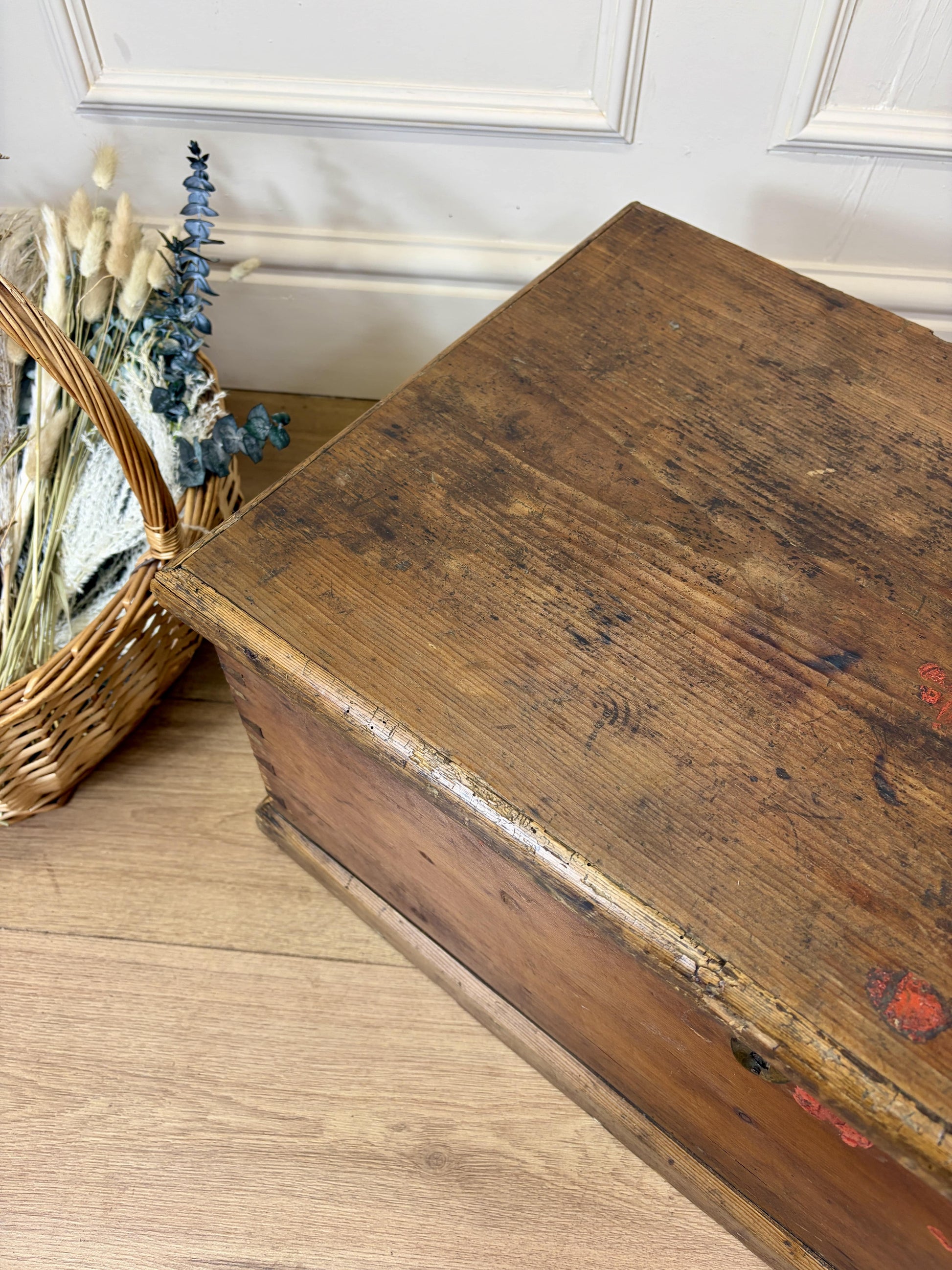 Vintage wooden trunk on a wooden floor with a wicker basket and decorative items in the background.