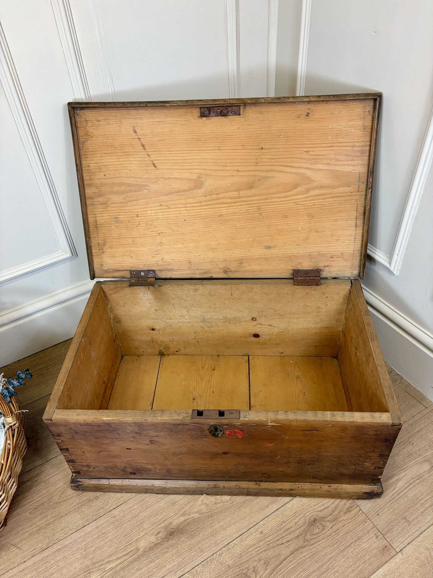 Wooden trunk on a wooden floor with a white paneled wall in the background