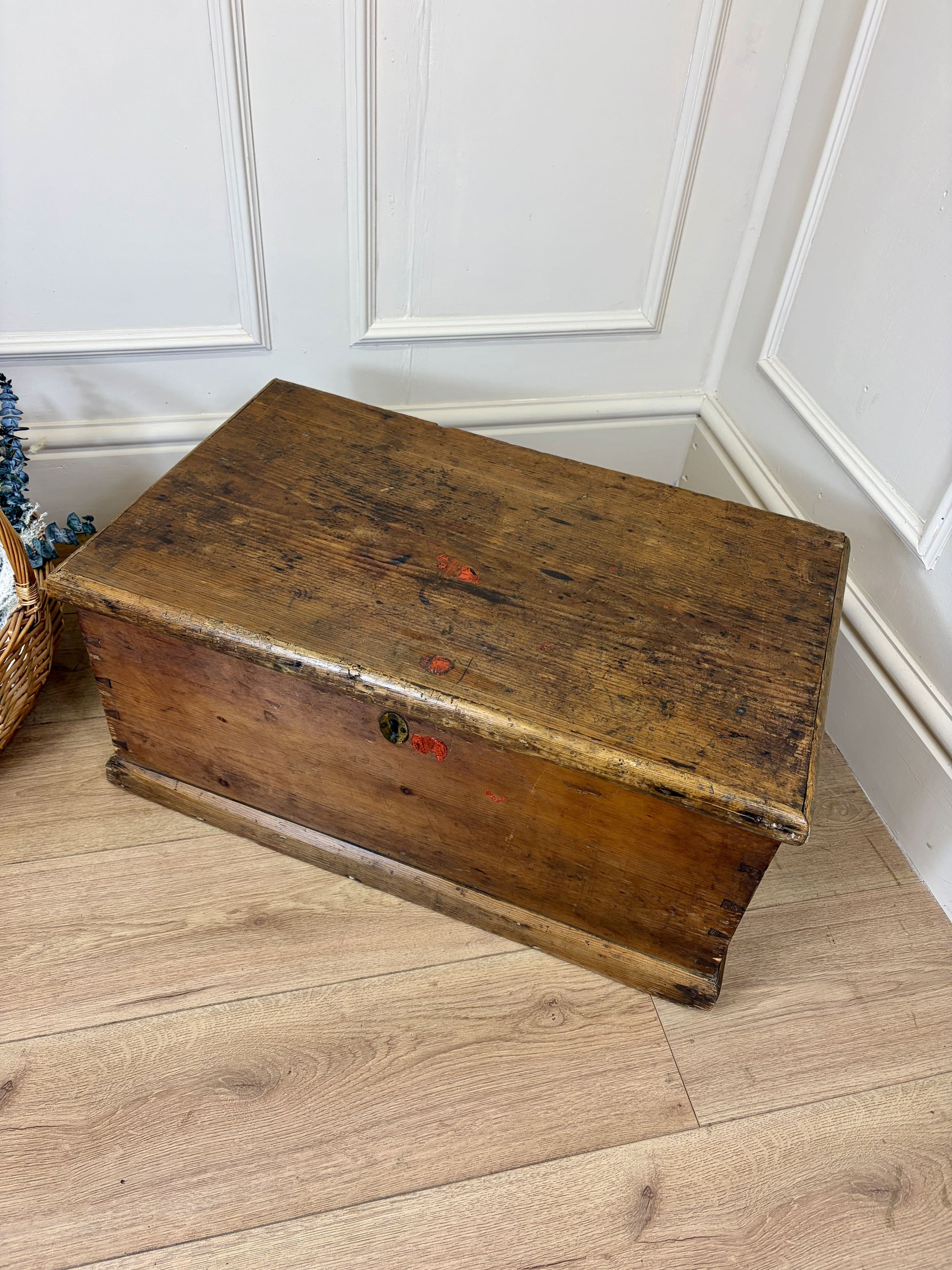 Vintage wooden trunk on a wooden floor against a white paneled wall.