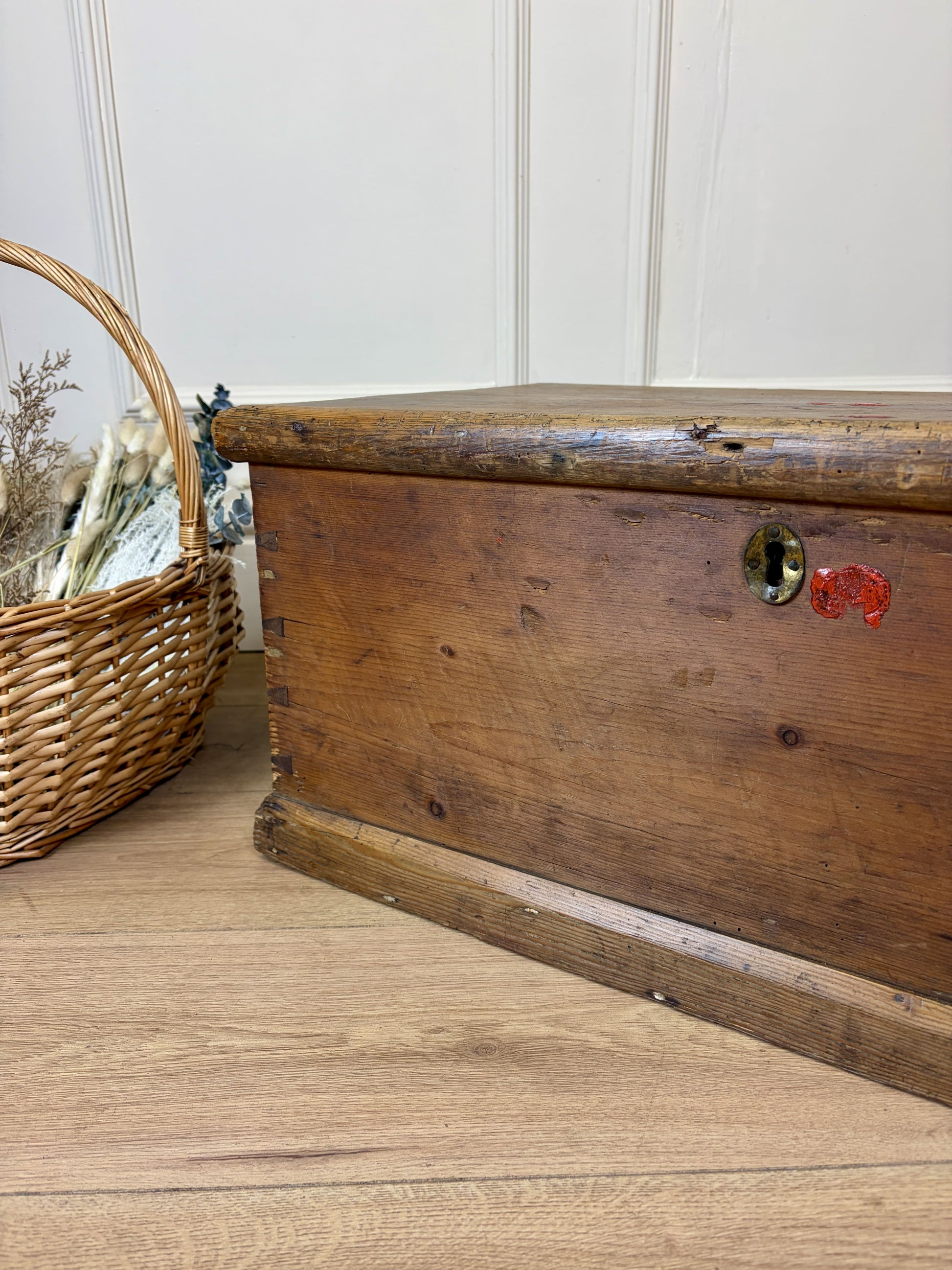 Wooden trunk with a wicker basket on a wooden floor against a white wall.