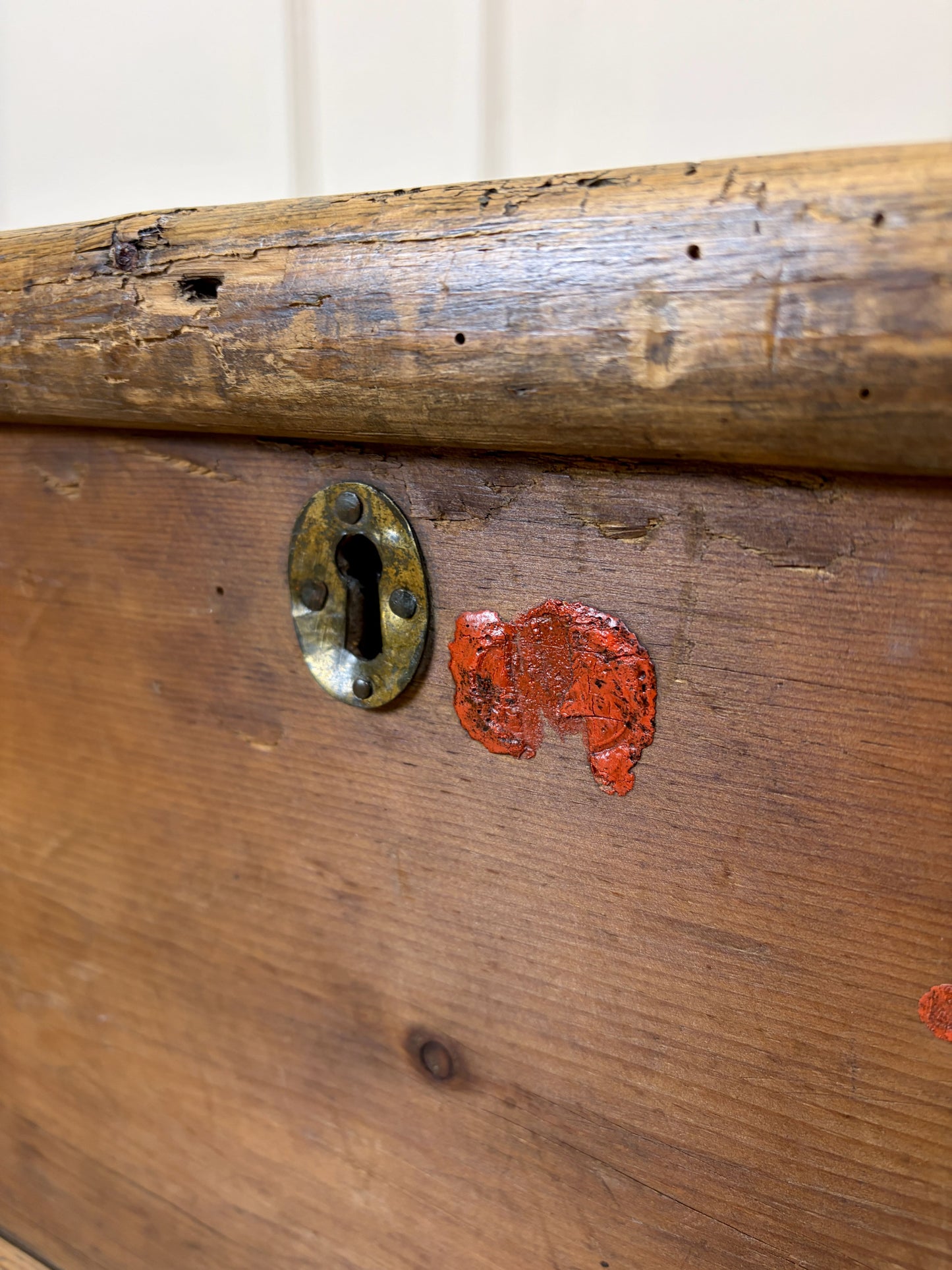 Close-up of an old wooden door with a brass lock and red paint chipping off.