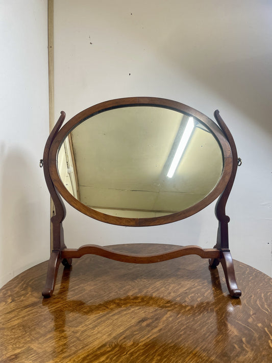 Wooden oval mirror on a stand against a white wall