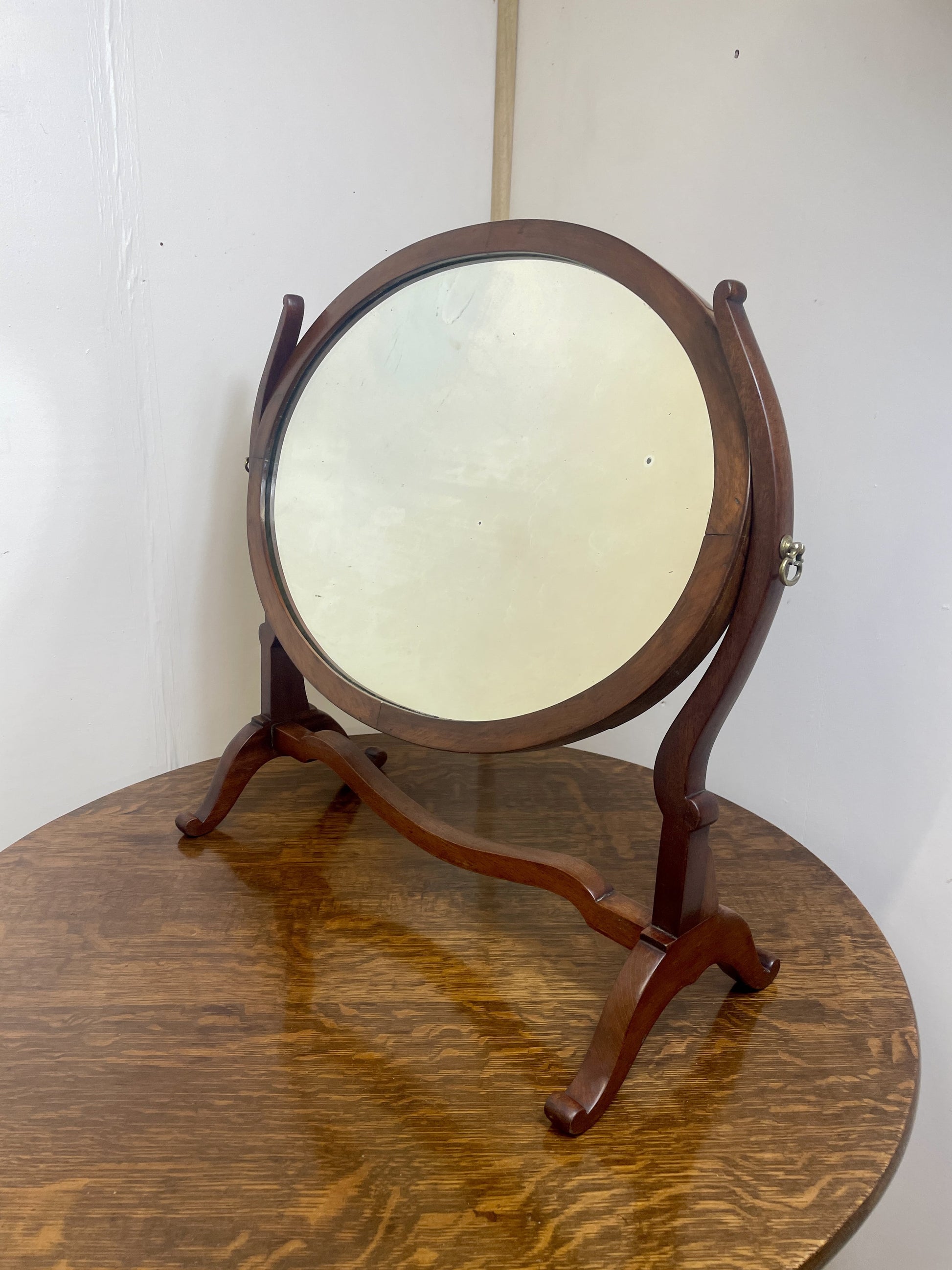 Wooden stand mirror on a wooden surface with a white wall background
