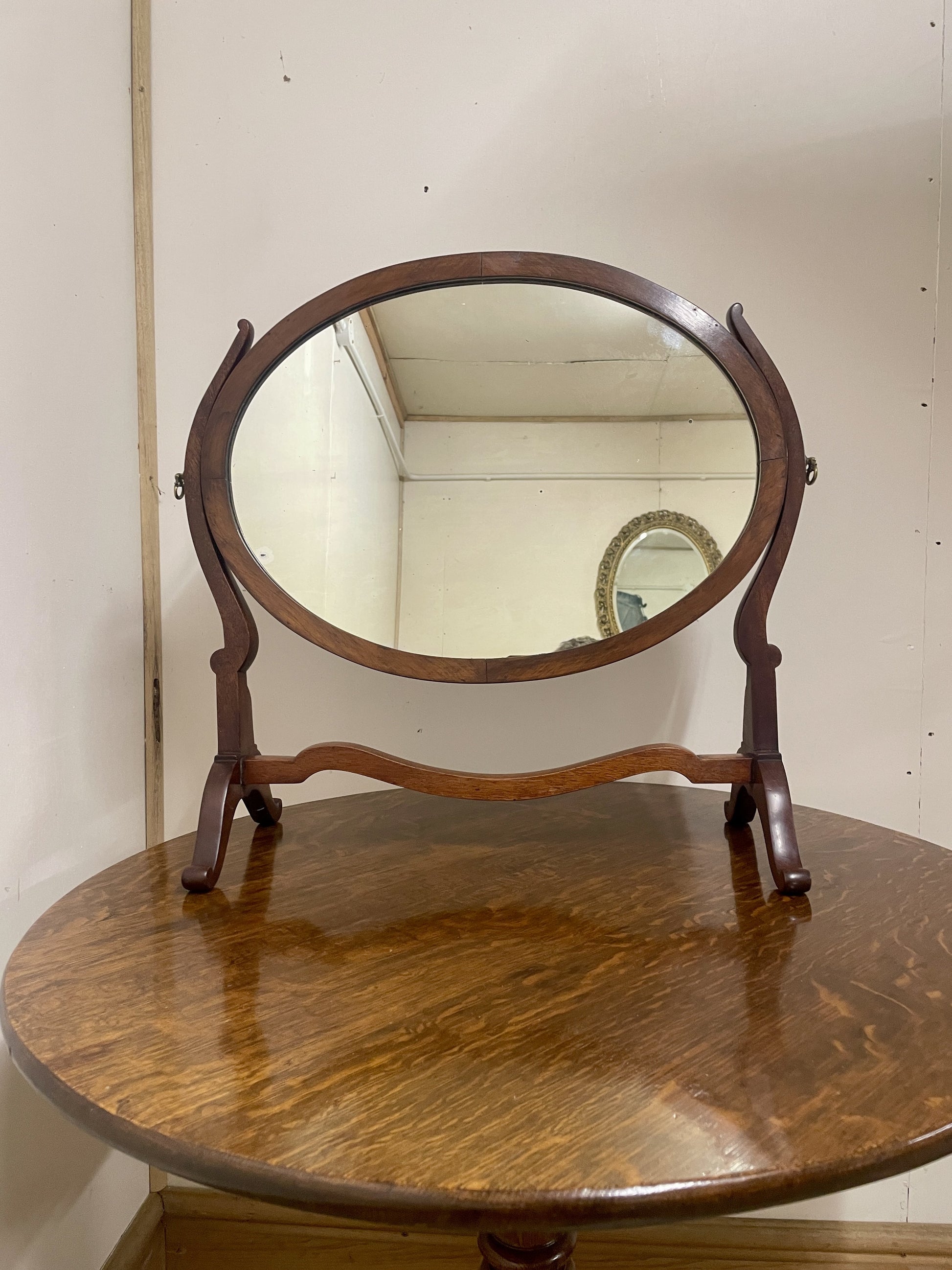 Wooden oval mirror on a round wooden table against a white wall.