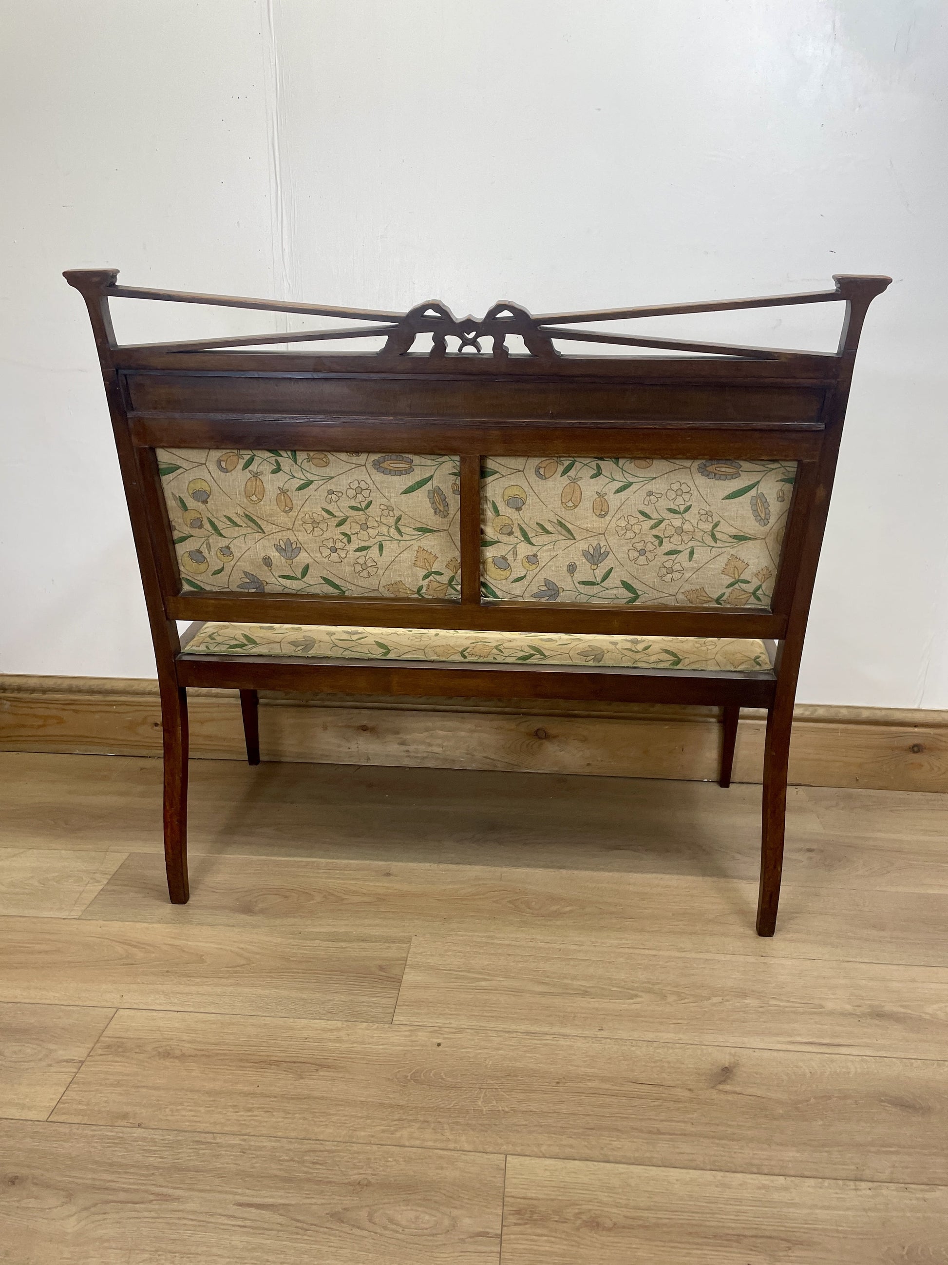 Wooden bench with floral-patterned cushion on a wooden floor against a white wall