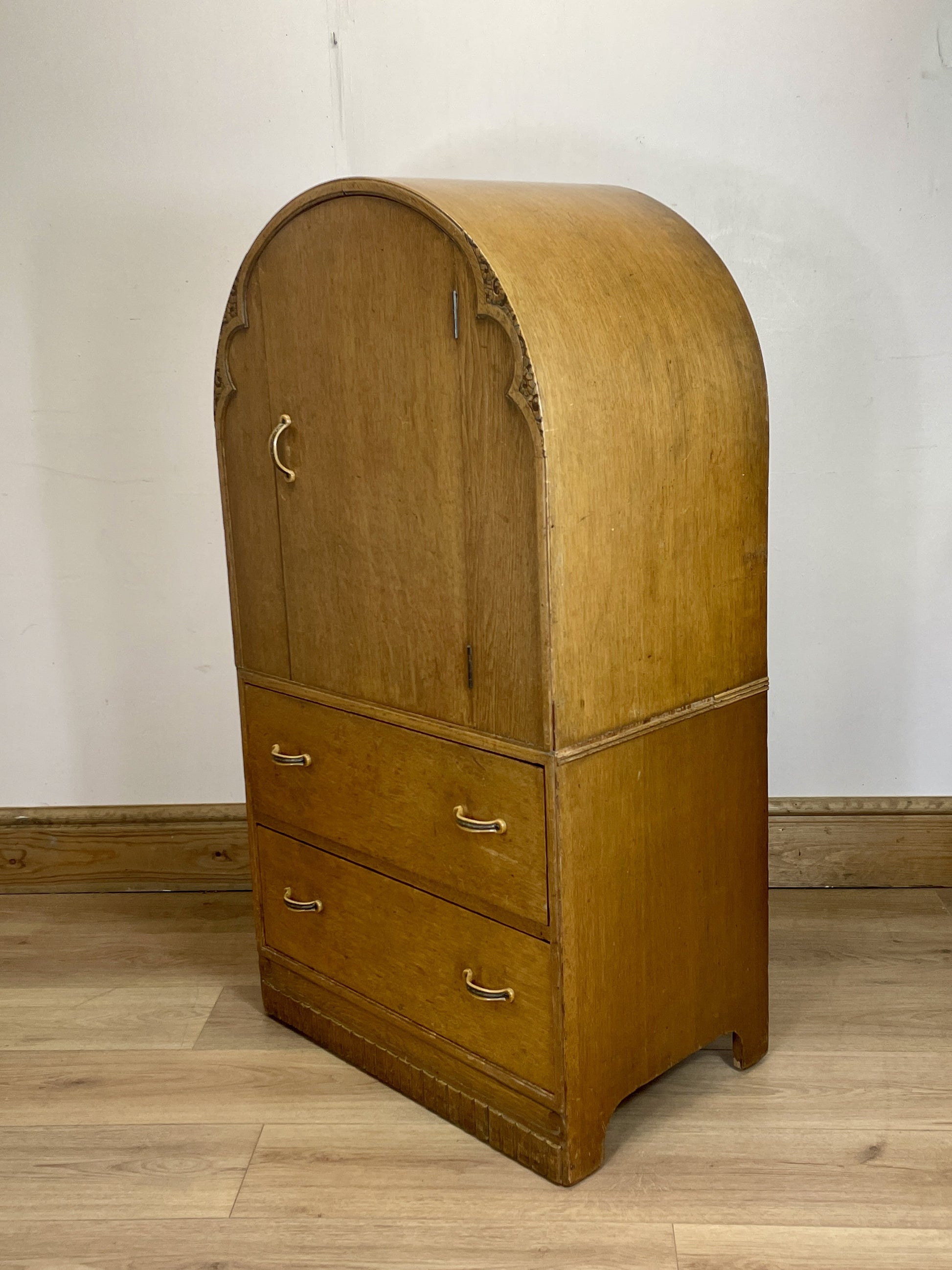 Wooden armoire with curved top and drawers on a wooden floor.