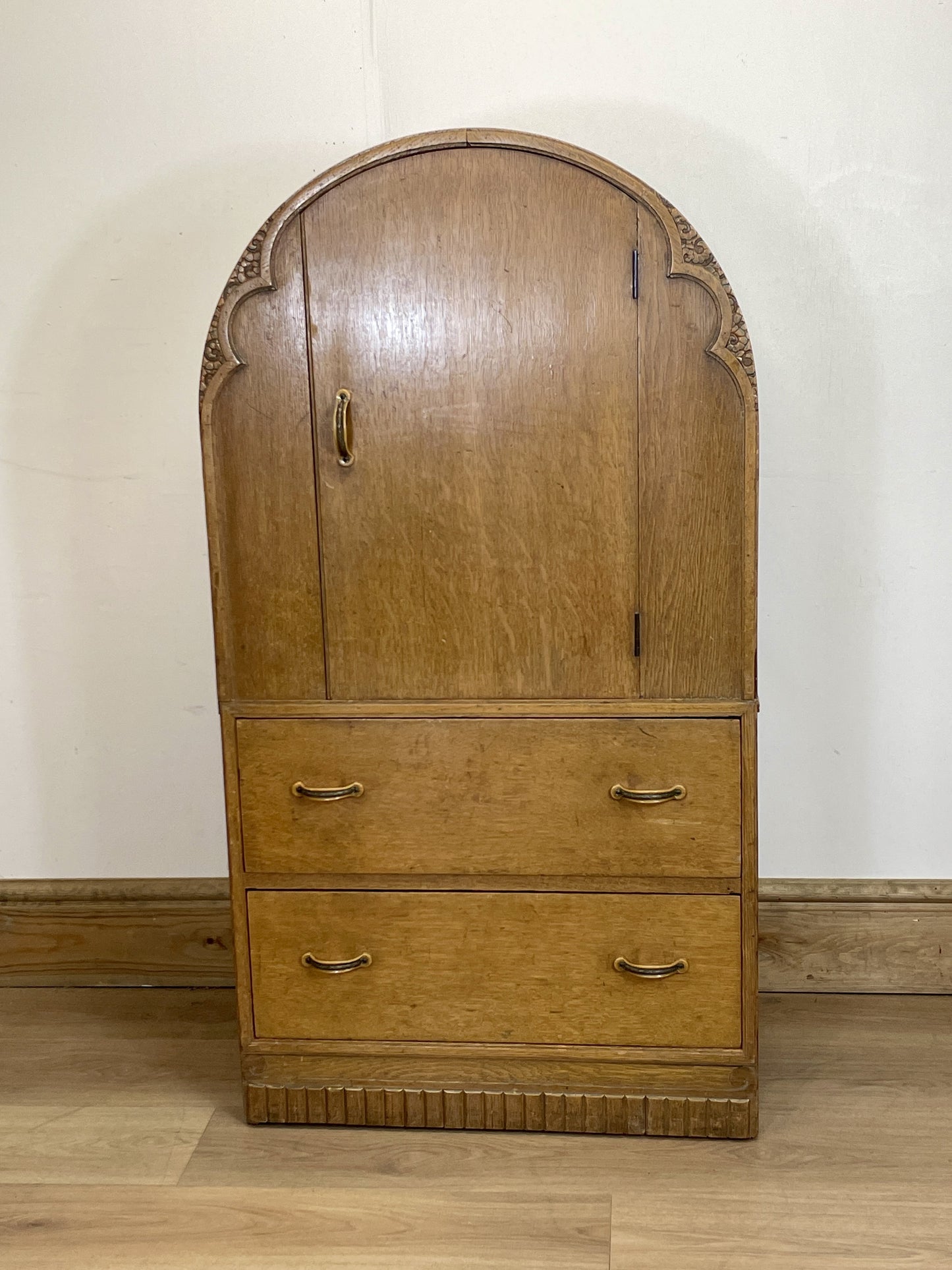 Wooden wardrobe with arched top and three drawers on a wooden floor.