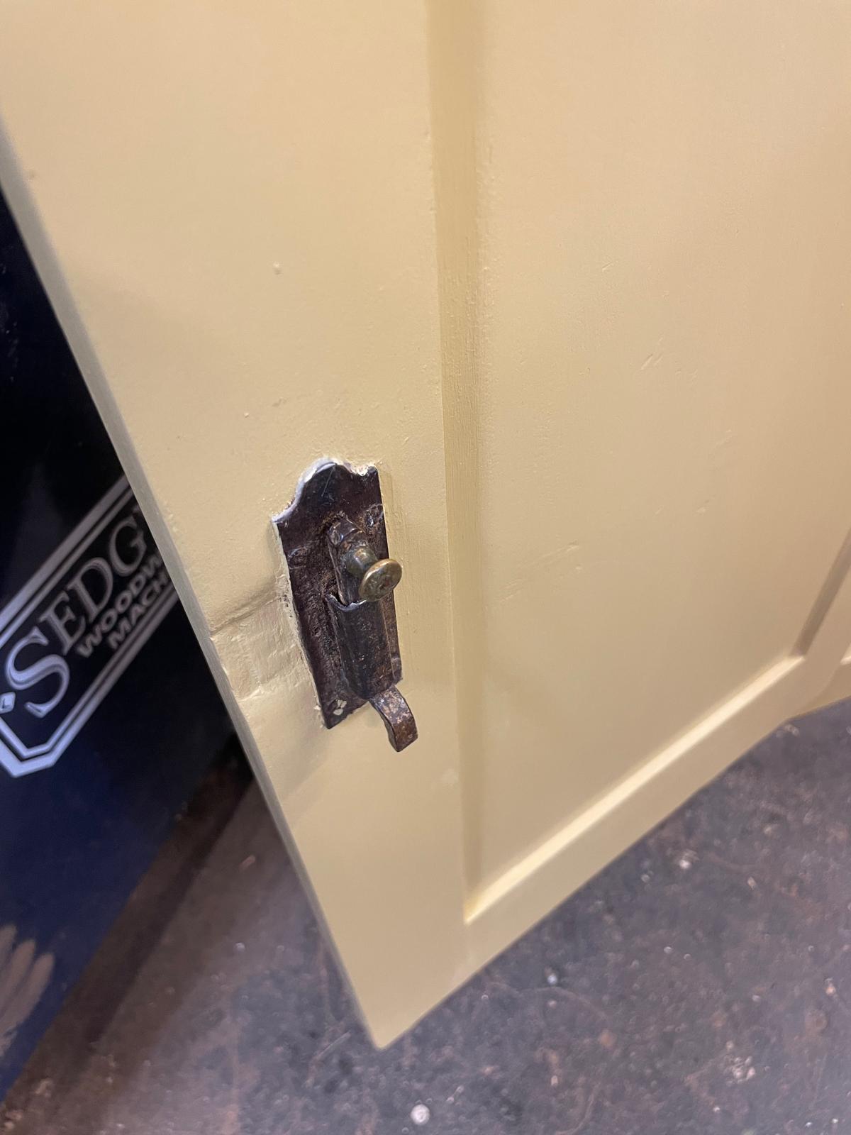 Close-up of a beige cabinet door with a metal handle and lock, blurred background.