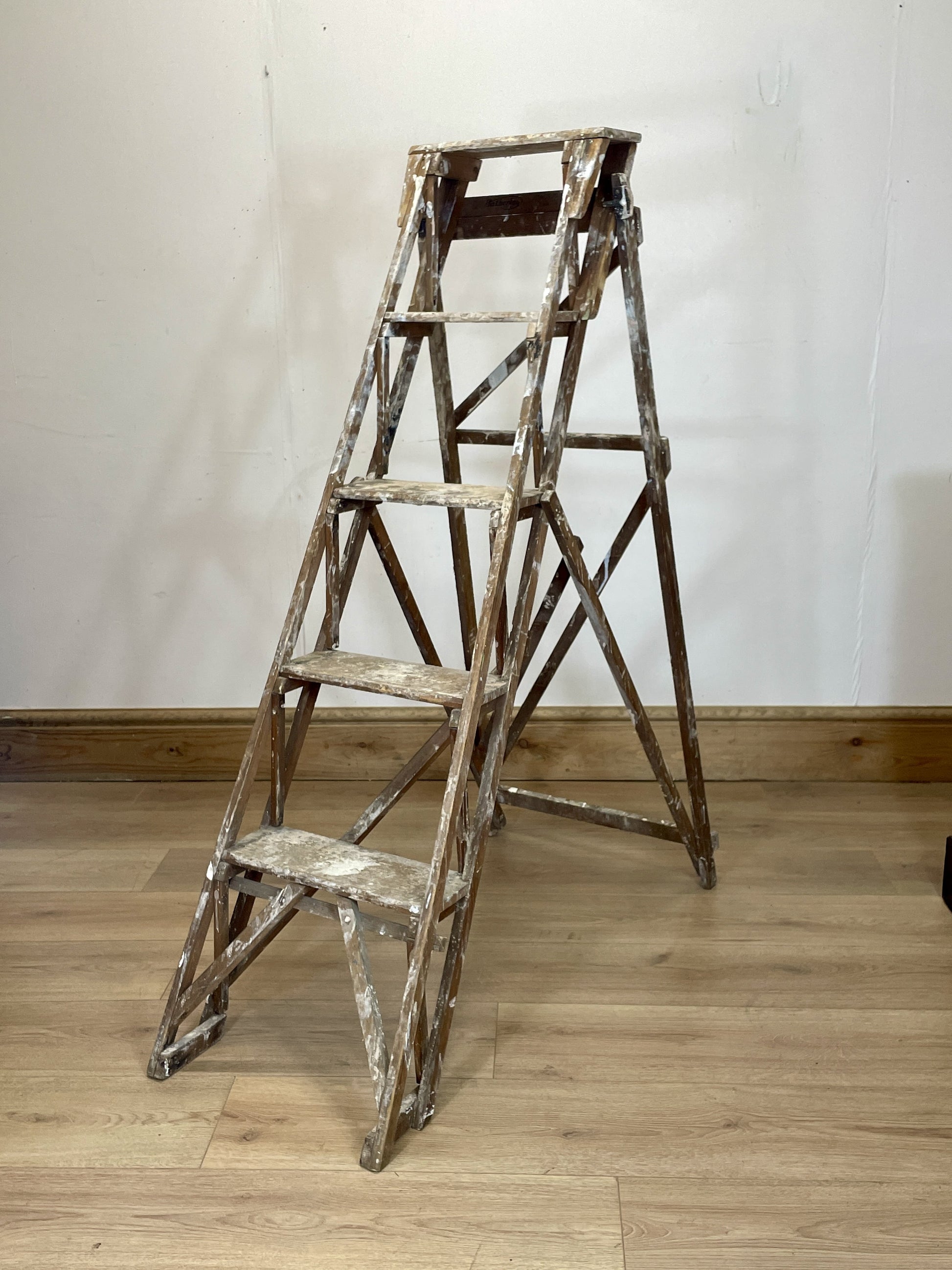 Vintage wooden step ladder against a white wall on a wooden floor