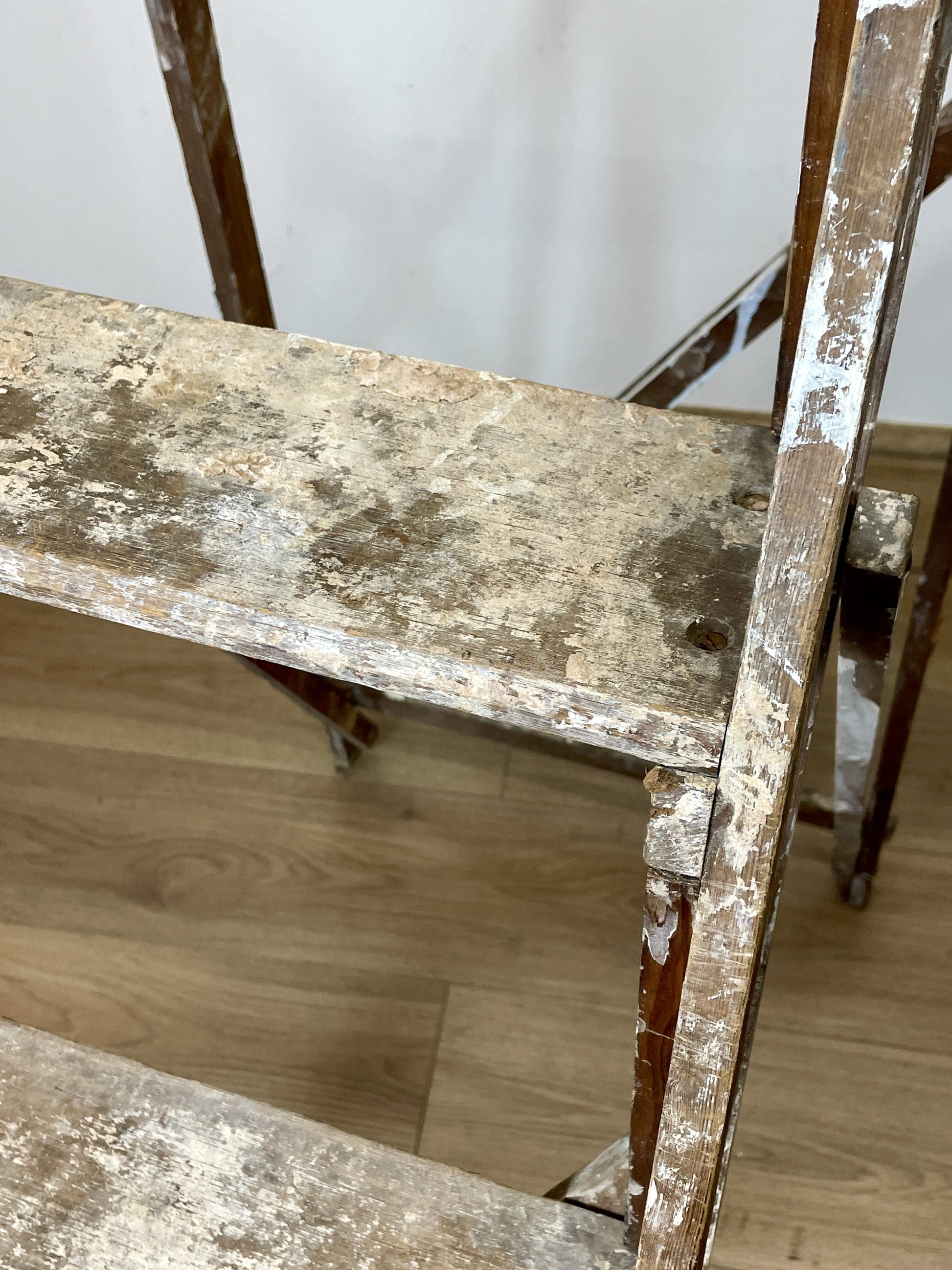 Worn wooden shelf with peeling paint on a light wood floor.