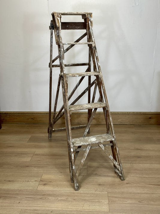 Vintage wooden step ladder against a white wall on a wooden floor
