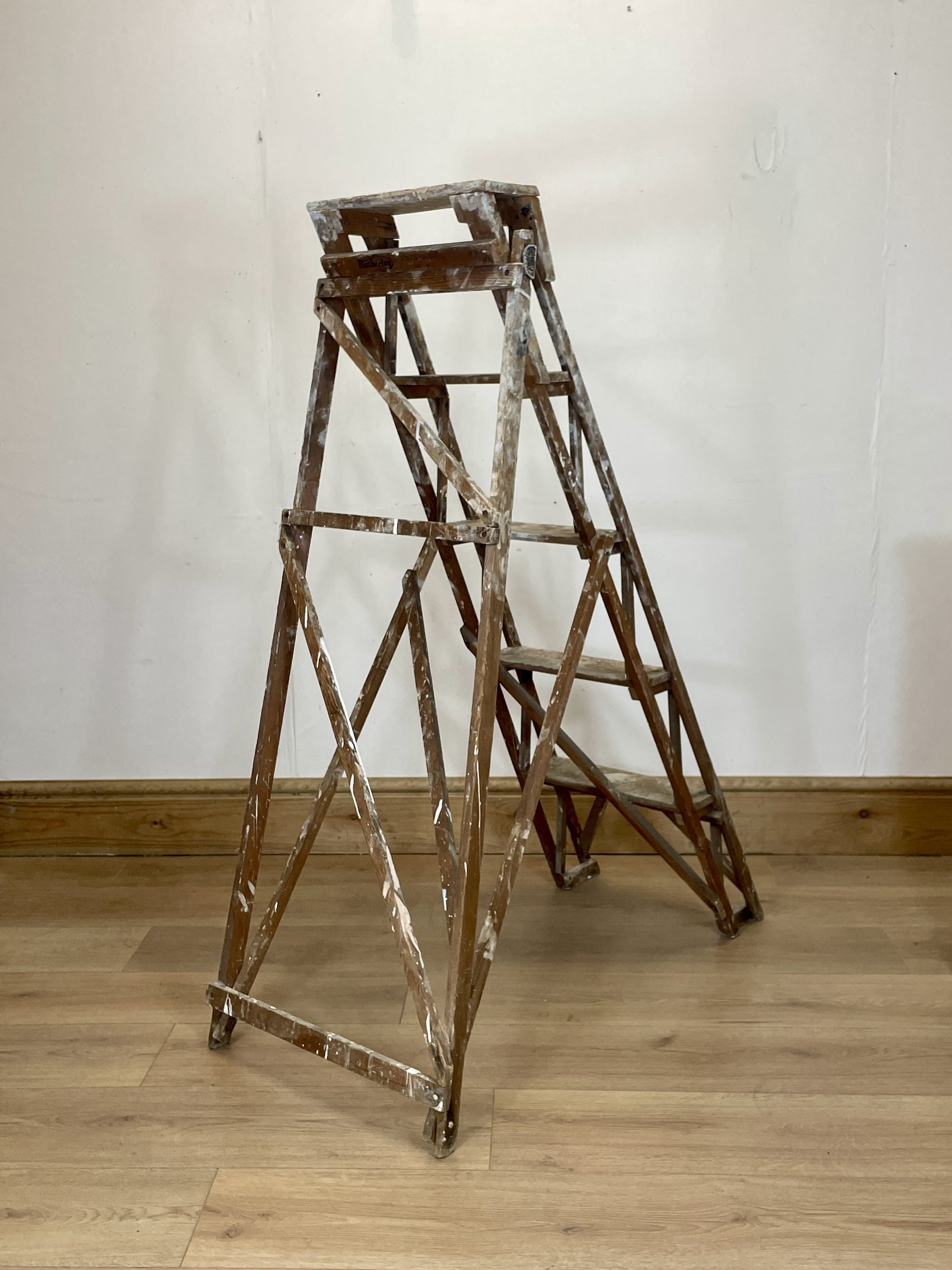 Vintage wooden step ladder against a white wall on a wooden floor
